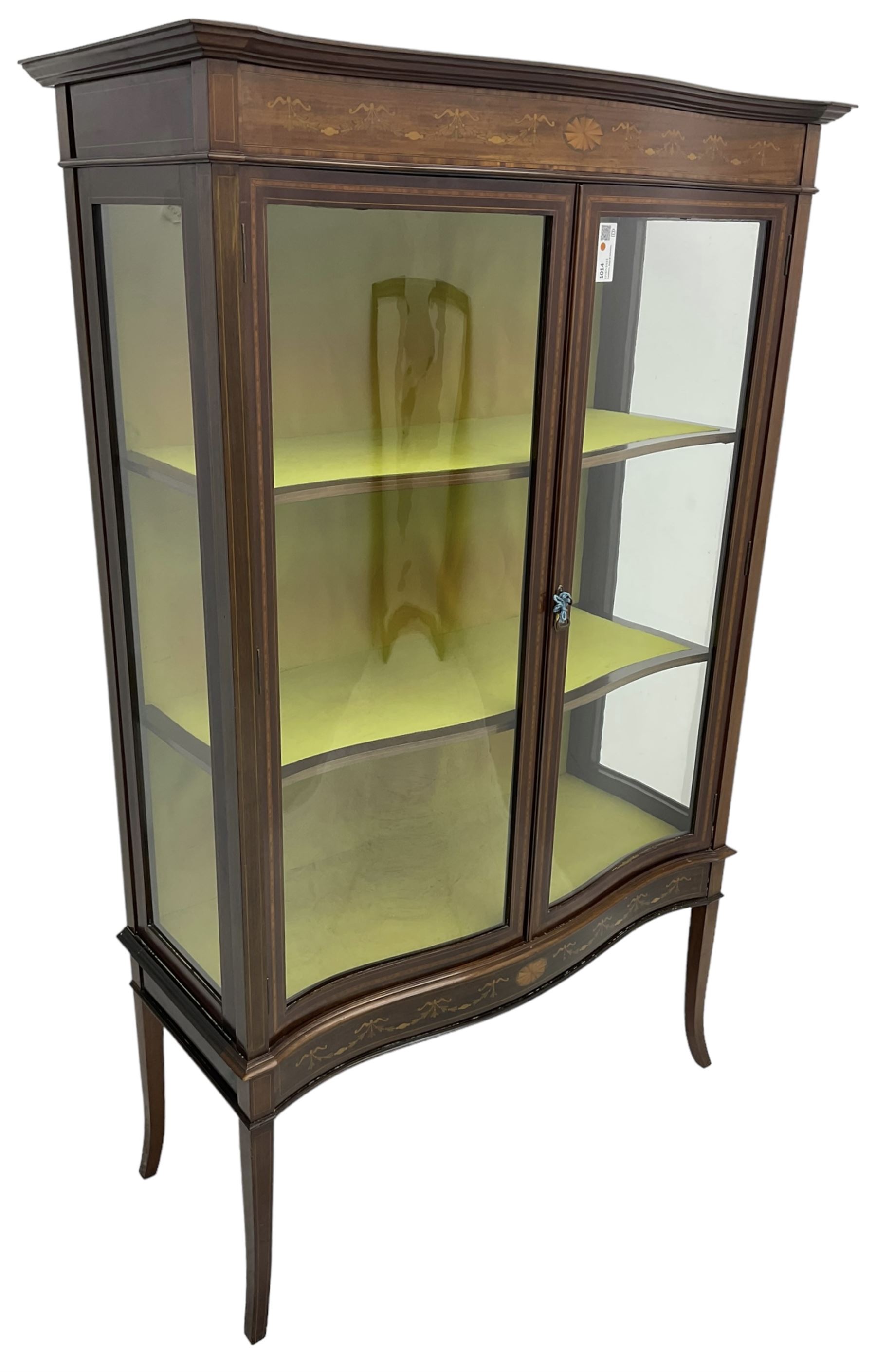 Edwardian inlaid mahogany serpentine display cabinet, projecting moulded cornice over figured frieze inlaid with tailing bellflowers and central fan motif, enclosed by two glazed doors, on square tapering supports with splayed terminals 