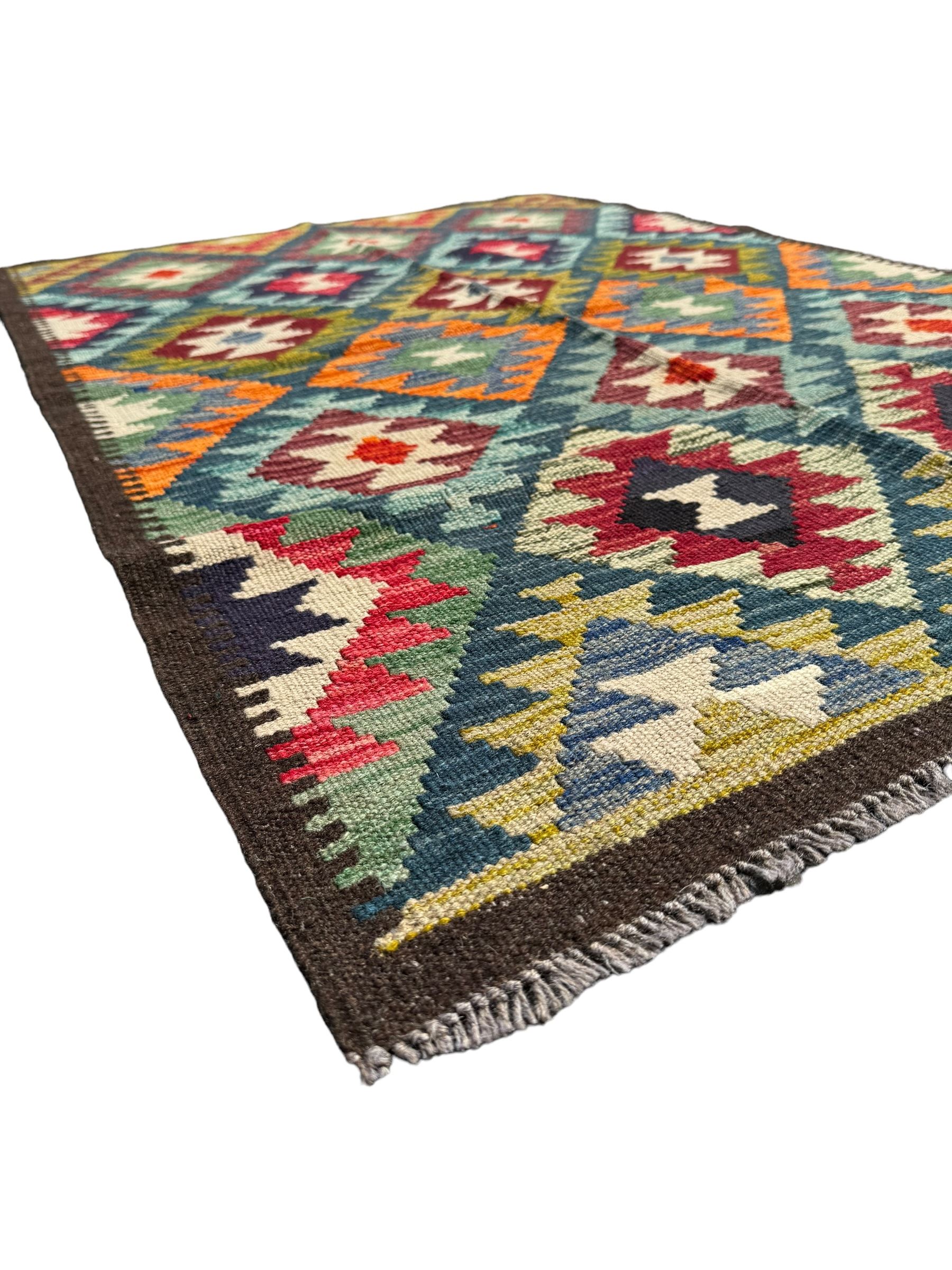 Maximana Kilim ground rug, the field decorated with a geometric pattern of multi-coloured diamonds and triangles, each containing stylised motifs, enclosed by a plain brown border