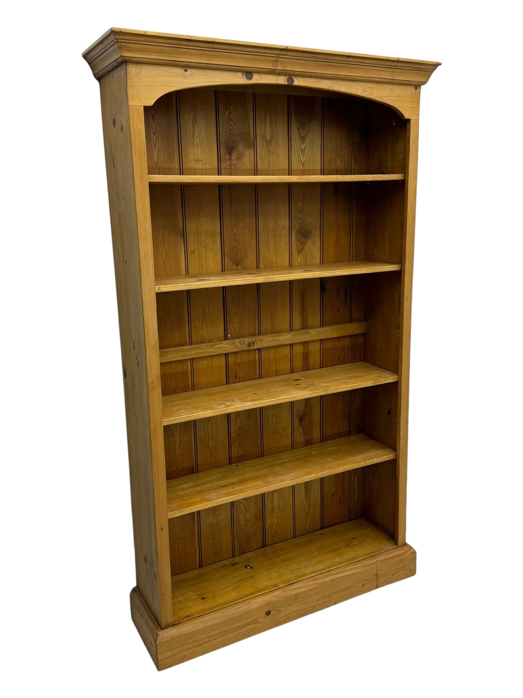 Pine open bookcase, projecting moulded cornice over arched frieze, fitted with four adjustable shelves, on plinth base