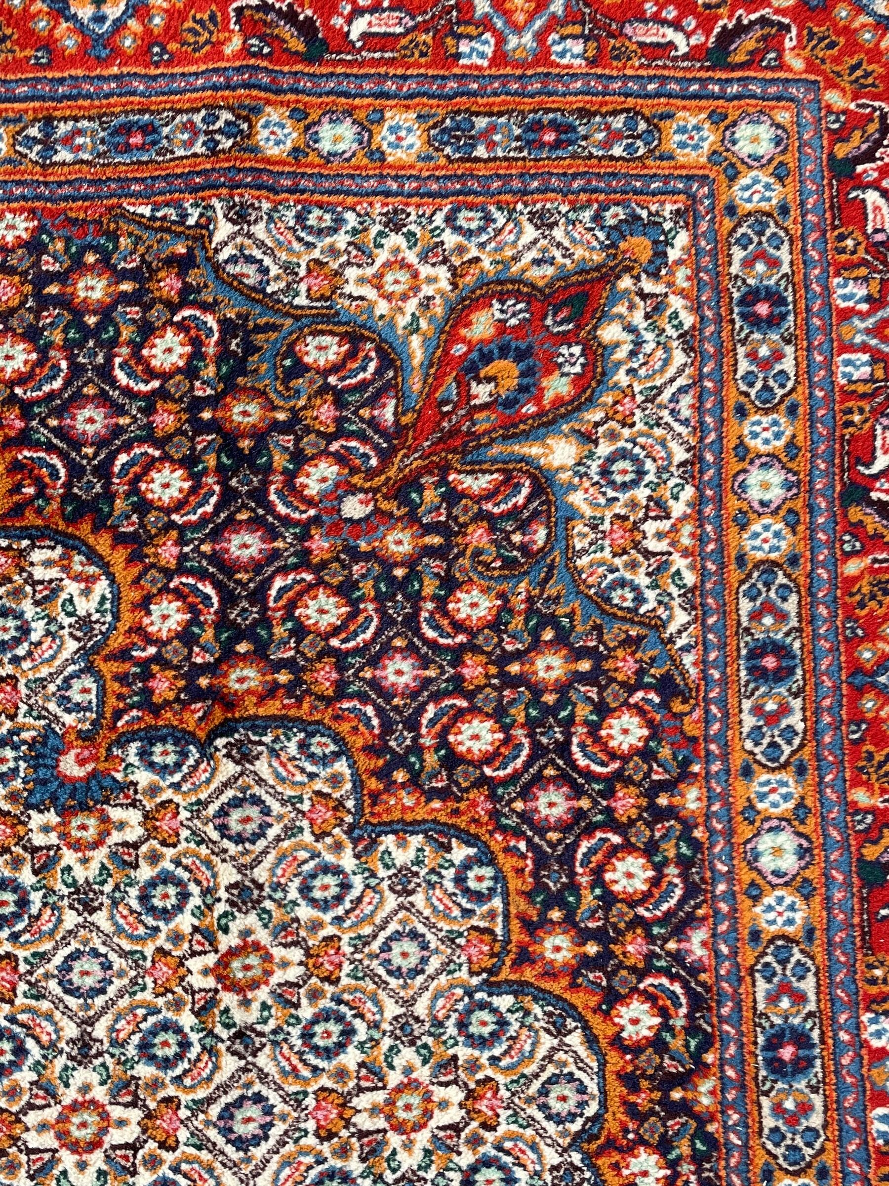 Persian Bidjar ivory and indigo ground rug, large central rosette medallion surrounded by floral herati motifs, crimson ground border decorated with repeating palmettes, within guard stripes decorated with small flower head motifs 