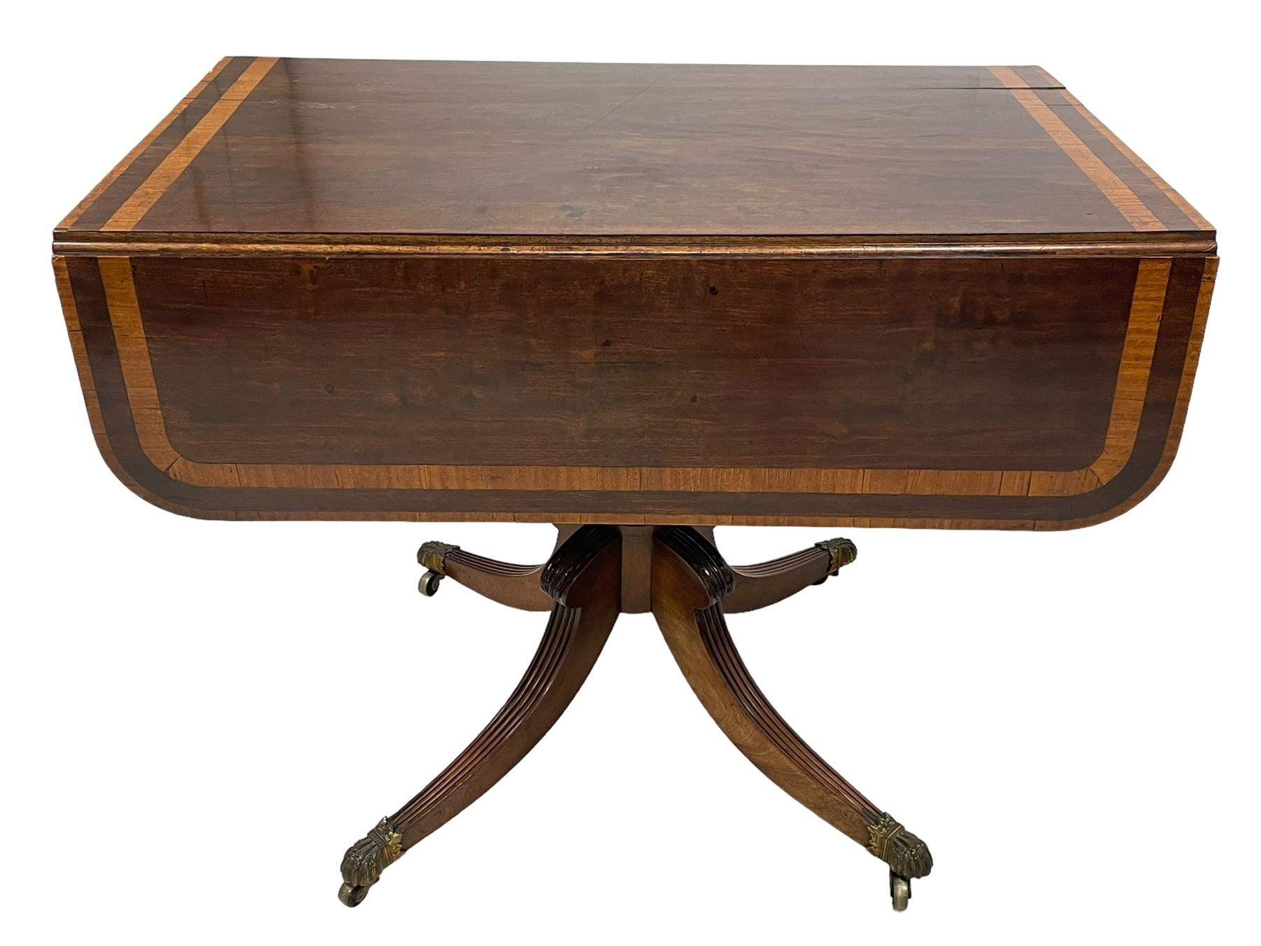 Early 19th century mahogany Pembroke table, rectangular drop-leaf top with rounded corners inlaid satinwood bands, single end drawer and opposing false drawer, turned pedestal on four acanthus carved and reed moulded splayed supports, cast brass cups and castors 