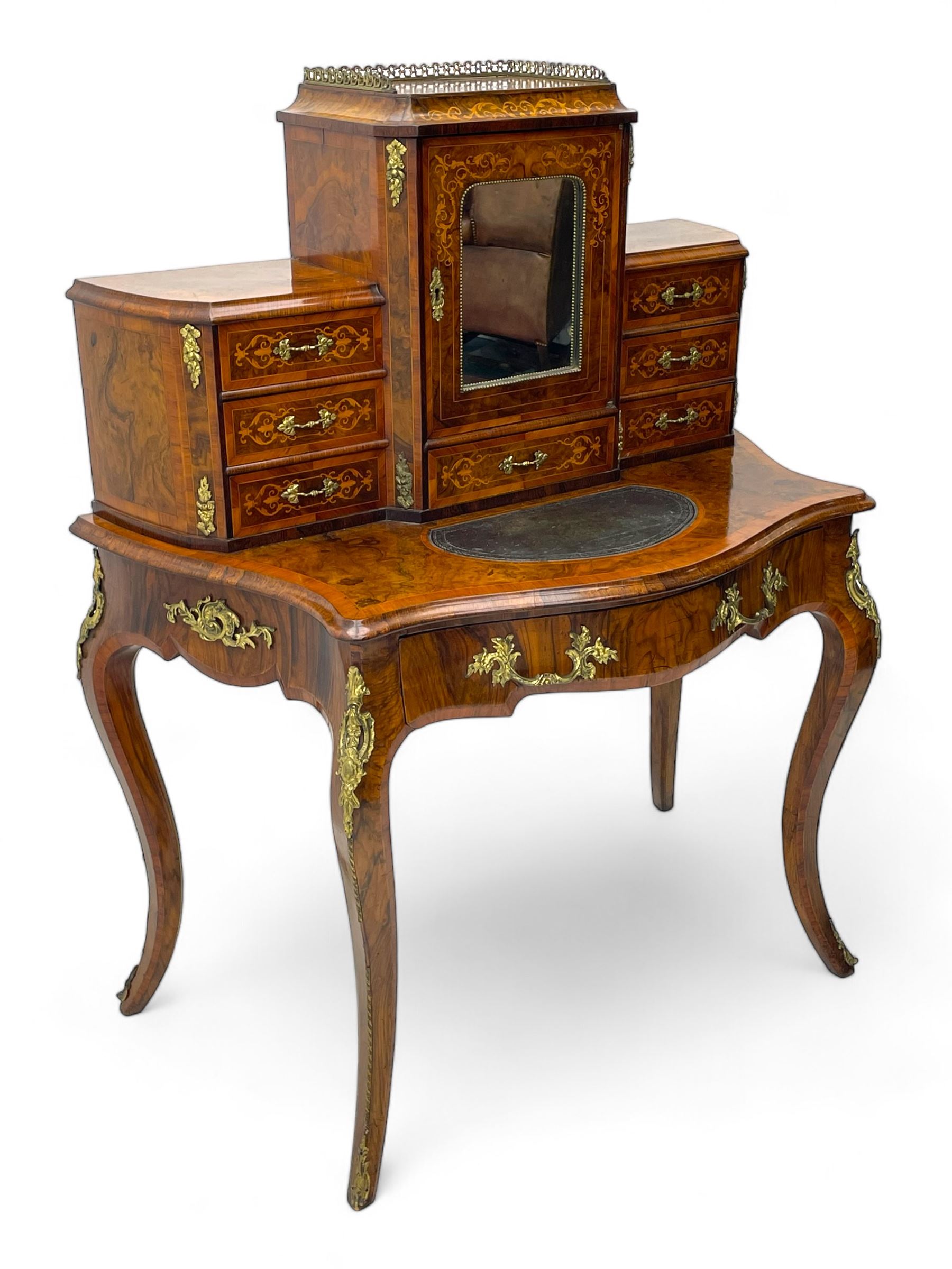 19th century French figured walnut Bonheur de Jour or writing desk, the upper section with brass gallery over mirror glazed cupboard and a combination of drawers, shaped and moulded top with leather inset and satinwood band, fitted with single drawer, on cabriole supports, inlaid throughout with scrolling foliate decoration in boxwood, ornate cast brass mounts 