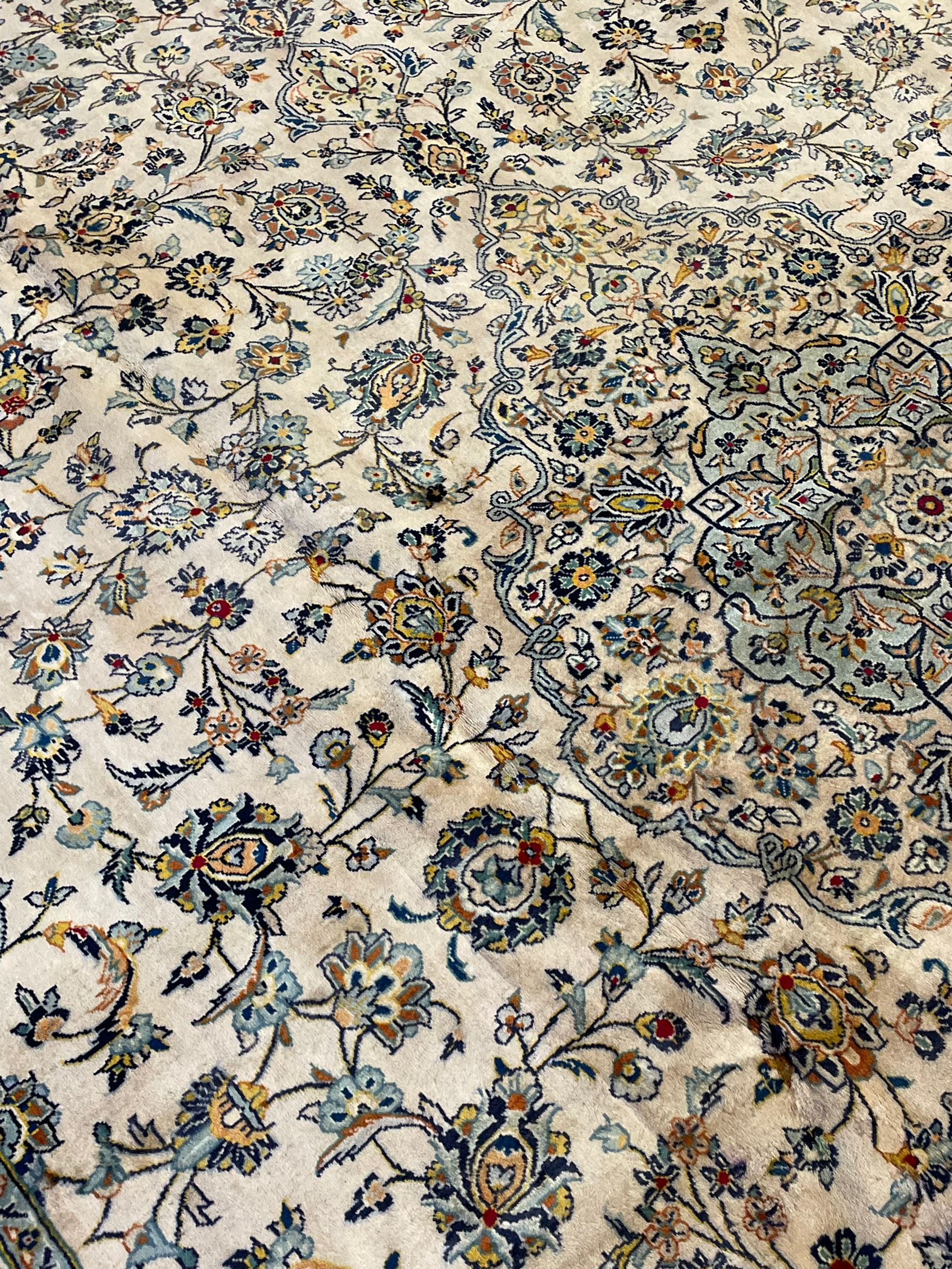 Central Persian Kashan pale khaki ground carpet, shaped central medallion enclosing small stylised motifs, the field decorated profusely with trailing foliate branches and plant motifs, guarded border with repeating floral design 