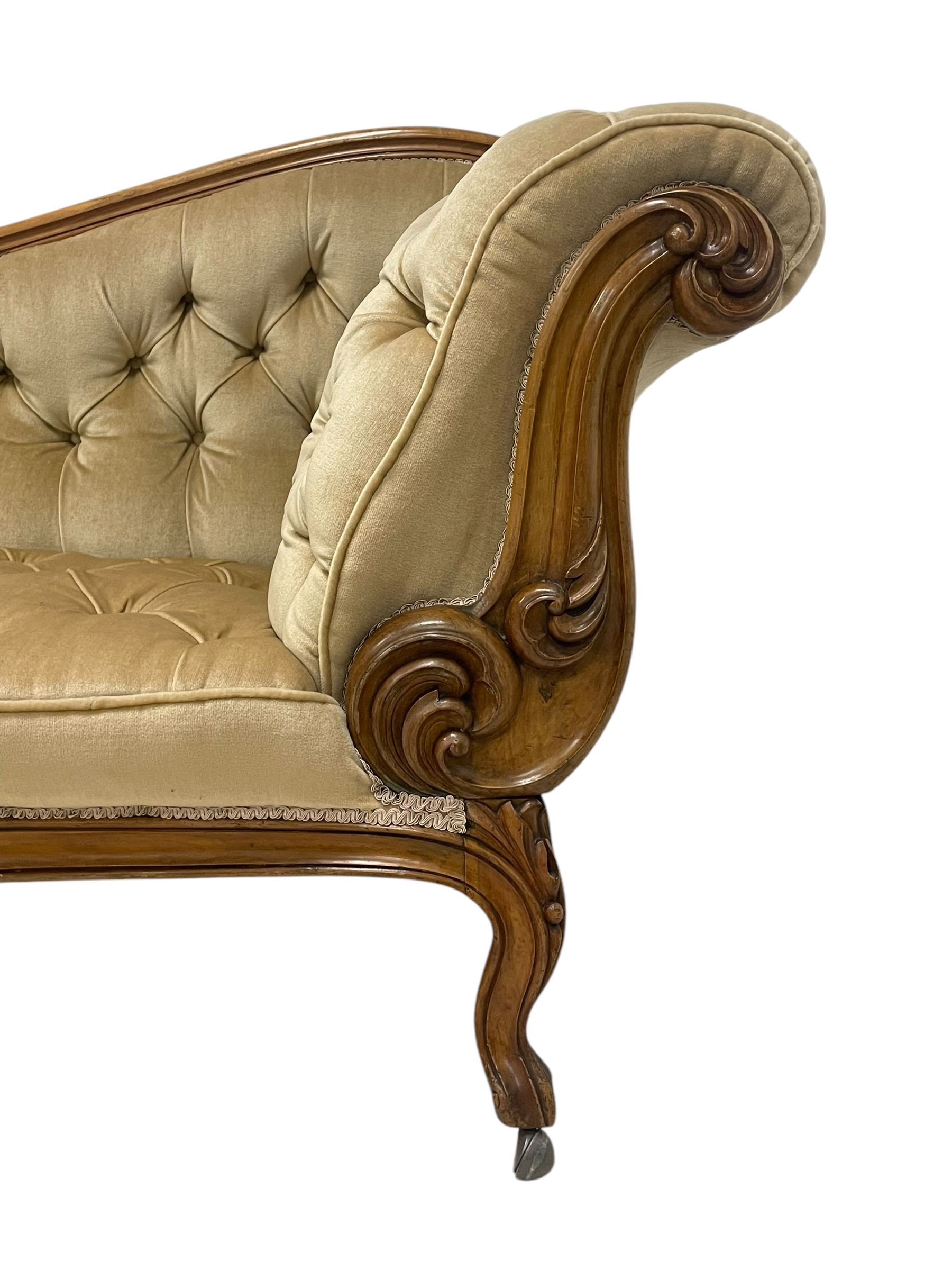 19th century walnut framed chaise longue, shaped back over scrolled arms decorated with moulded curling acanthus carvings, upholstered in deep buttoned champagne fabric, raised on cabriole supports with applied floral carved decoration, on castors