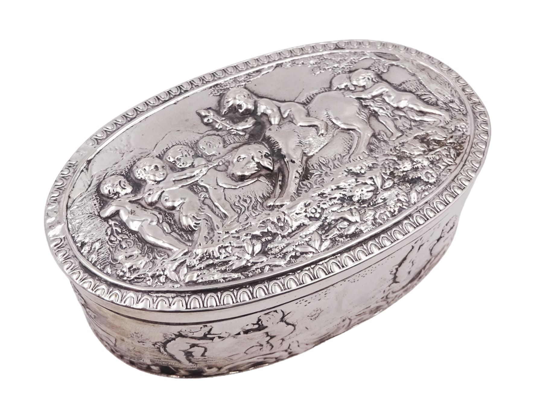 Late 19th century German Hanau silver box, of oval form, embossed throughout with putti in various scenes including riding a dog, playing instruments, pulling a cart and dancing, opening to reveal a gilt interior, with Hanau marks for B Neresheimer & Sohne, W9cm, H3cm