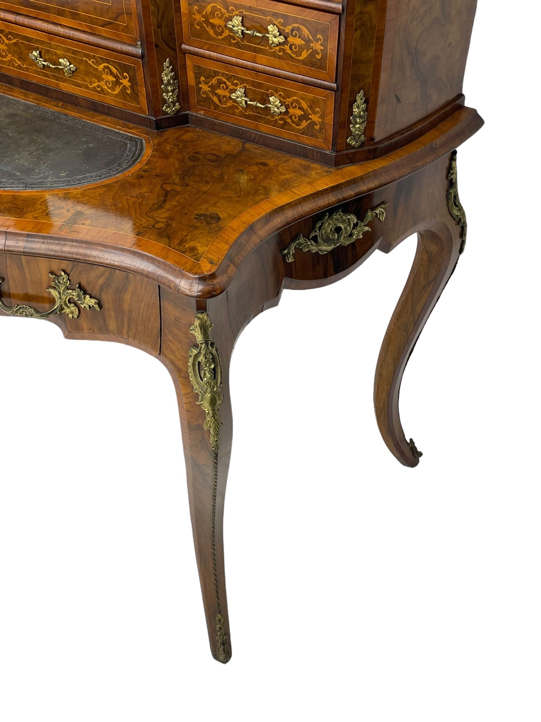 19th century French figured walnut Bonheur de Jour or writing desk, the upper section with brass gallery over mirror glazed cupboard and a combination of drawers, shaped and moulded top with leather inset and satinwood band, fitted with single drawer, on cabriole supports, inlaid throughout with scrolling foliate decoration in boxwood, ornate cast brass mounts 