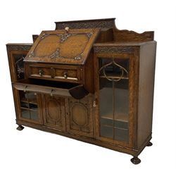 Early 20th century heavily carved oak bookcase bureau, raised back with grape-vine carved frieze, over fall-front enclosing fitted interior, above two short drawers and curved frieze drawer, flanked by astragal glazed and panelled cupboards, on turned feet