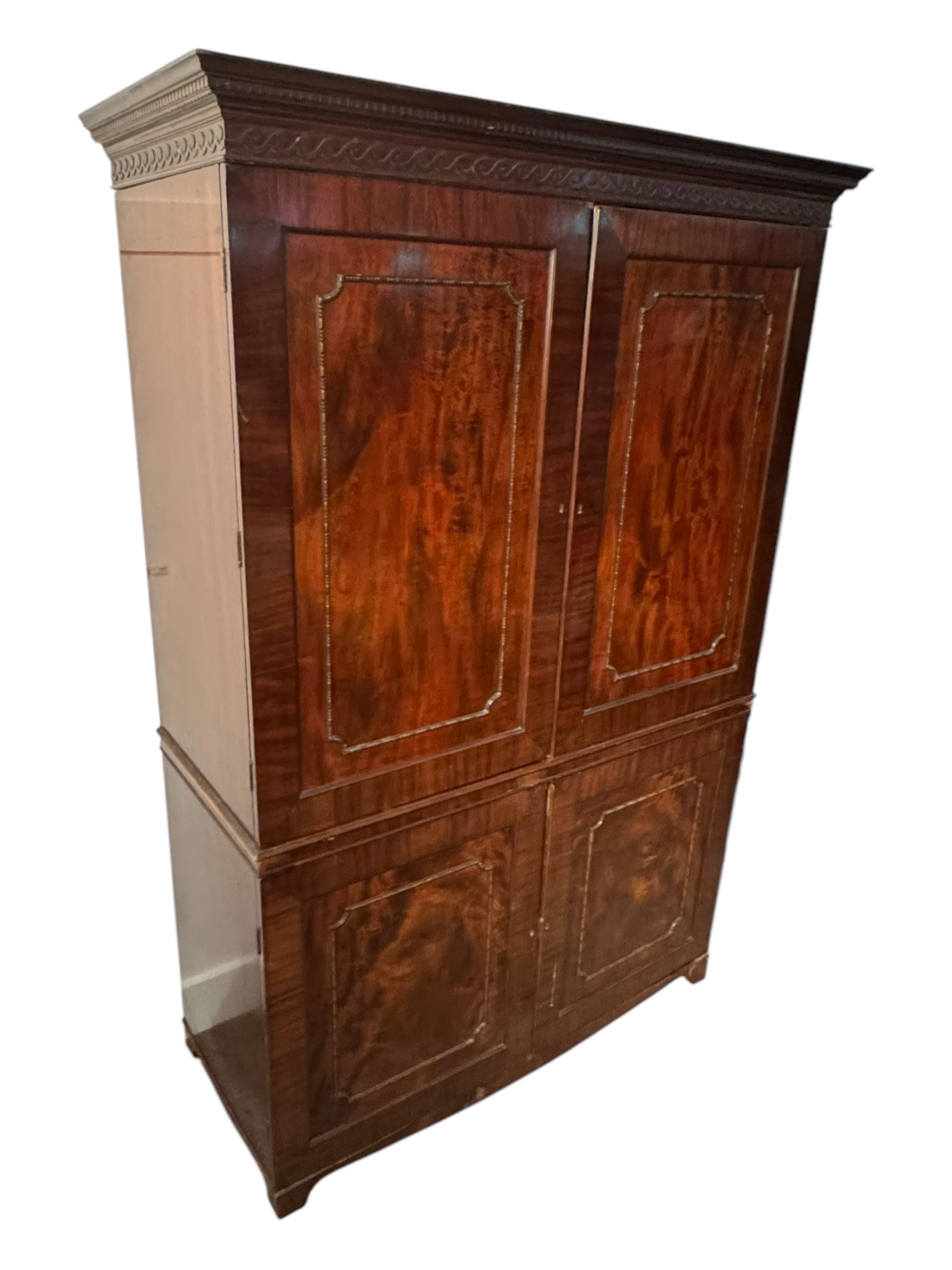 Victorian mahogany linen press, projecting cornice with dentil and scroll detailing, double panelled doors opening to an interior fitted with a brass hanging rail and coat hooks, lower section with two drawers and fitted shelves for additional storage, raised on bracket feet