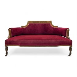 Late Victorian inlaid walnut two seat settee, the shaped cresting rail decorated with foliate inlays and boxwood stringing, upholstered in crimson velvet with sprung seat, raised on turned and fluted supports with ceramic castors