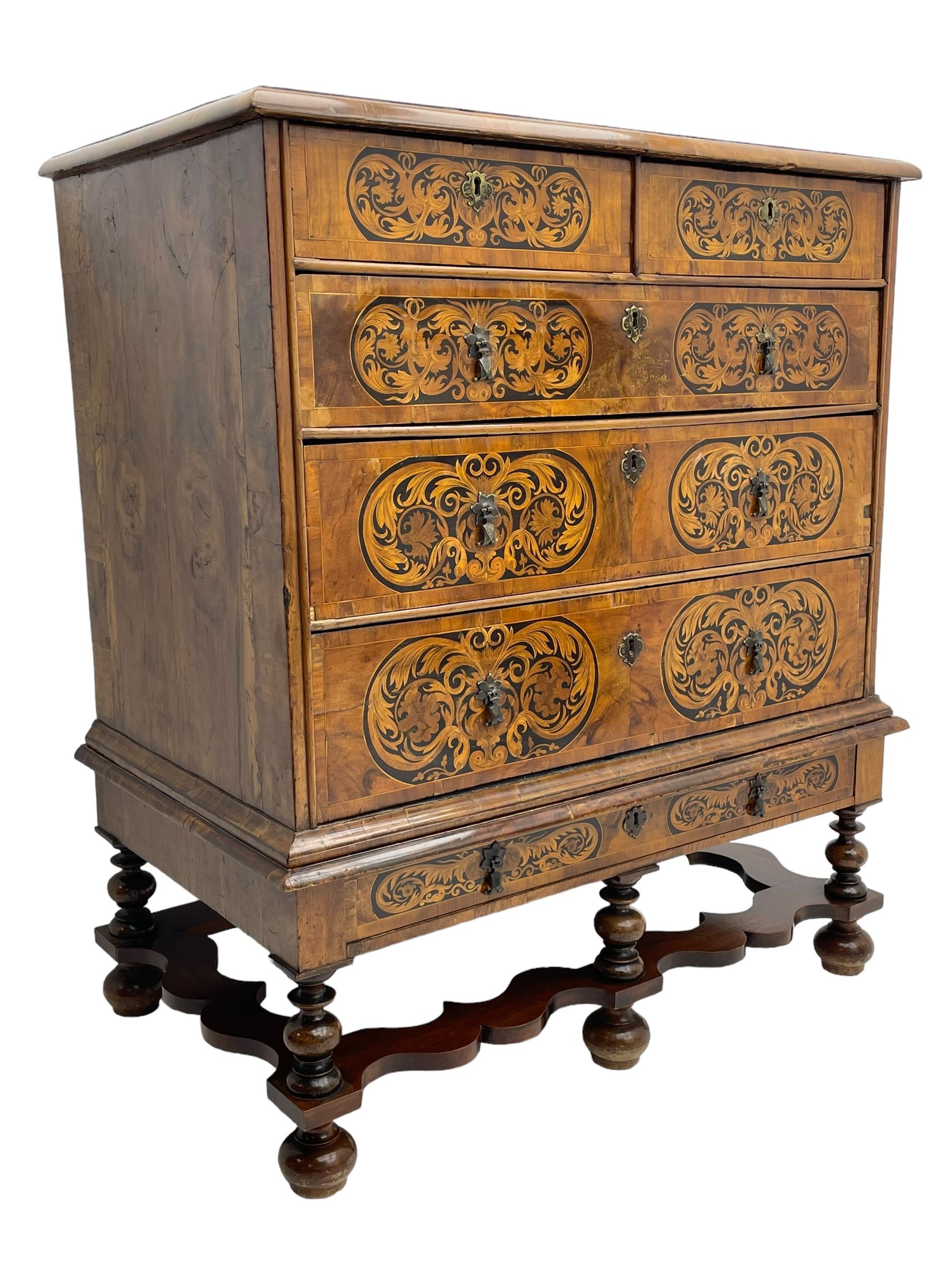 18th century inlaid walnut chest on stand, ovolo-moulded rectangular top inlaid with ebony panels each decorated with scrolling foliage, flower heads and birds, fitted with two short over three long drawers, the drawer fronts decorated with ebony panels enclosing curled leaf inlays, the base fitted with single drawer on turned supports united by waved stretchers, on turned bun feet 