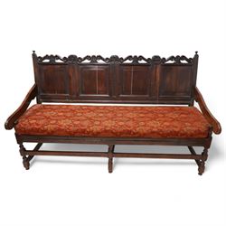 Early 18th century oak hall bench or settle, the cresting rail carved with S-scrolls and crown motifs, over a quadruple panelled back with carved rail, loose seat cushion upholstered in terracotta foliate fabric, flanked by shaped arm terminals, raised on turned supports united by stretchers