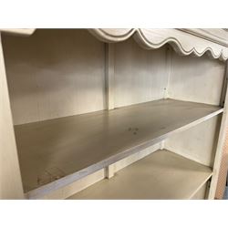 Provincial style cream painted bookcase, projecting cornice over dentil moulding, scalloped frieze above three open shelves, lower section fitted with two drawers, on bracket feet with apron