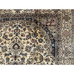 Persian Nain ivory ground carpet, central indigo medallion, the busy floral field decorated with scrolling vines and flower heads in shades of blue, beige, and red, wide guarded border with repeating palmettes and foliate motifs