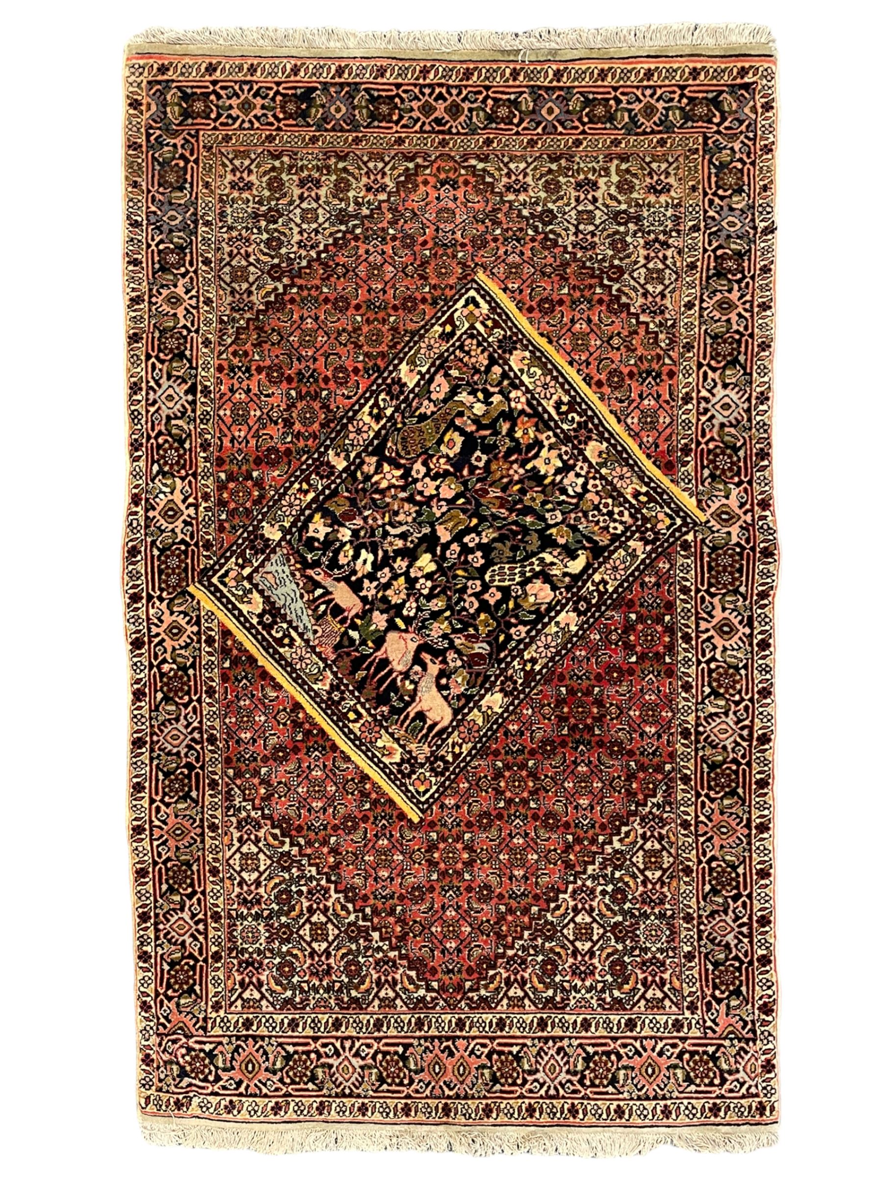 Persian Bidjar peach ground rug, the field decorated with repeating Herati motifs surrounding an off-centre lozenge medallion, decorated with grazing deer and peacock motids, the field border decorated with repeating stylised plant motifs, multiple floral design guard bands