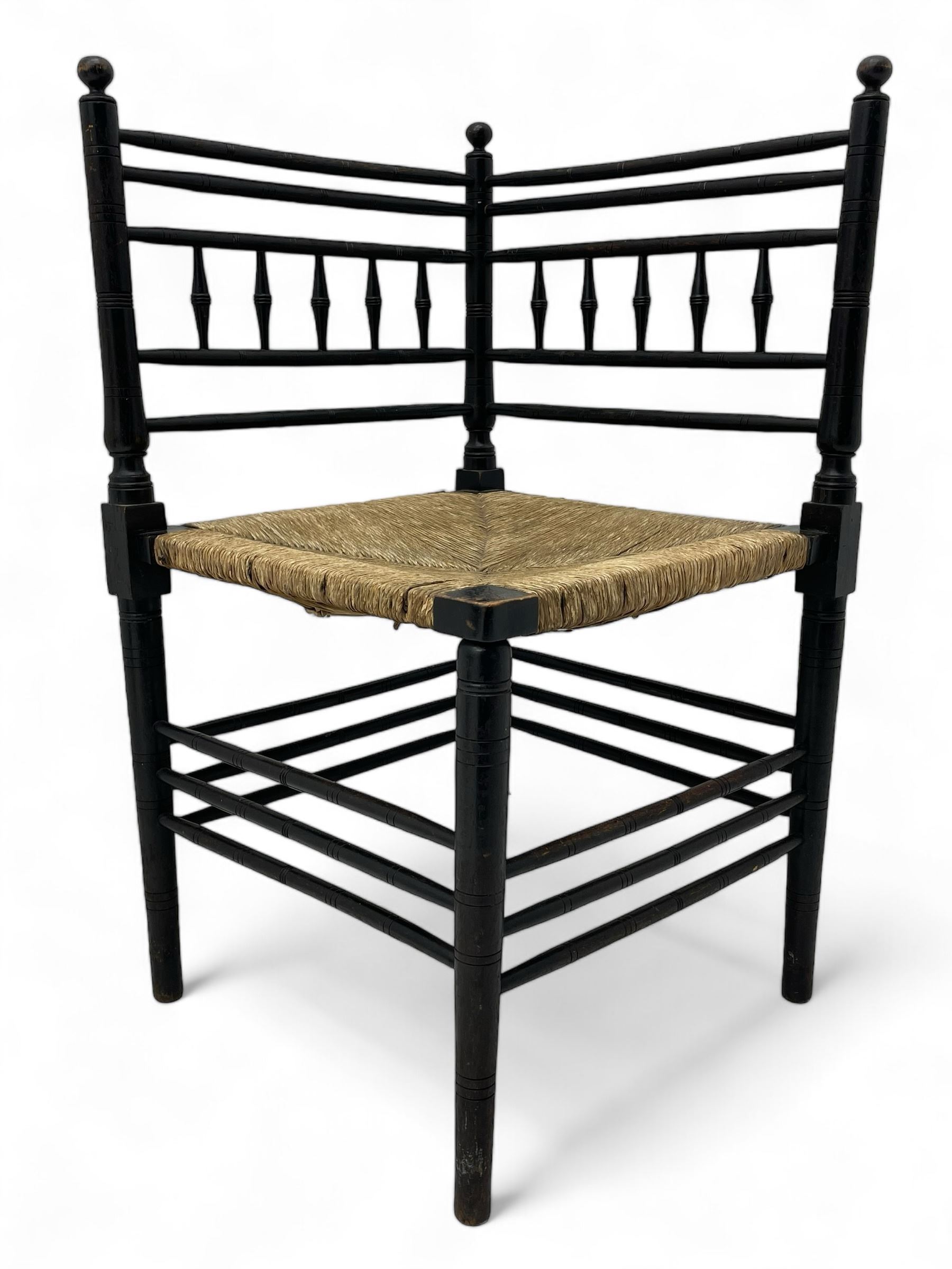 In the manner of William Morris - Arts & Crafts period corner chair, swell turned horizontal rails with balustrade back, rush seat on ring turned supports, black paint finish 