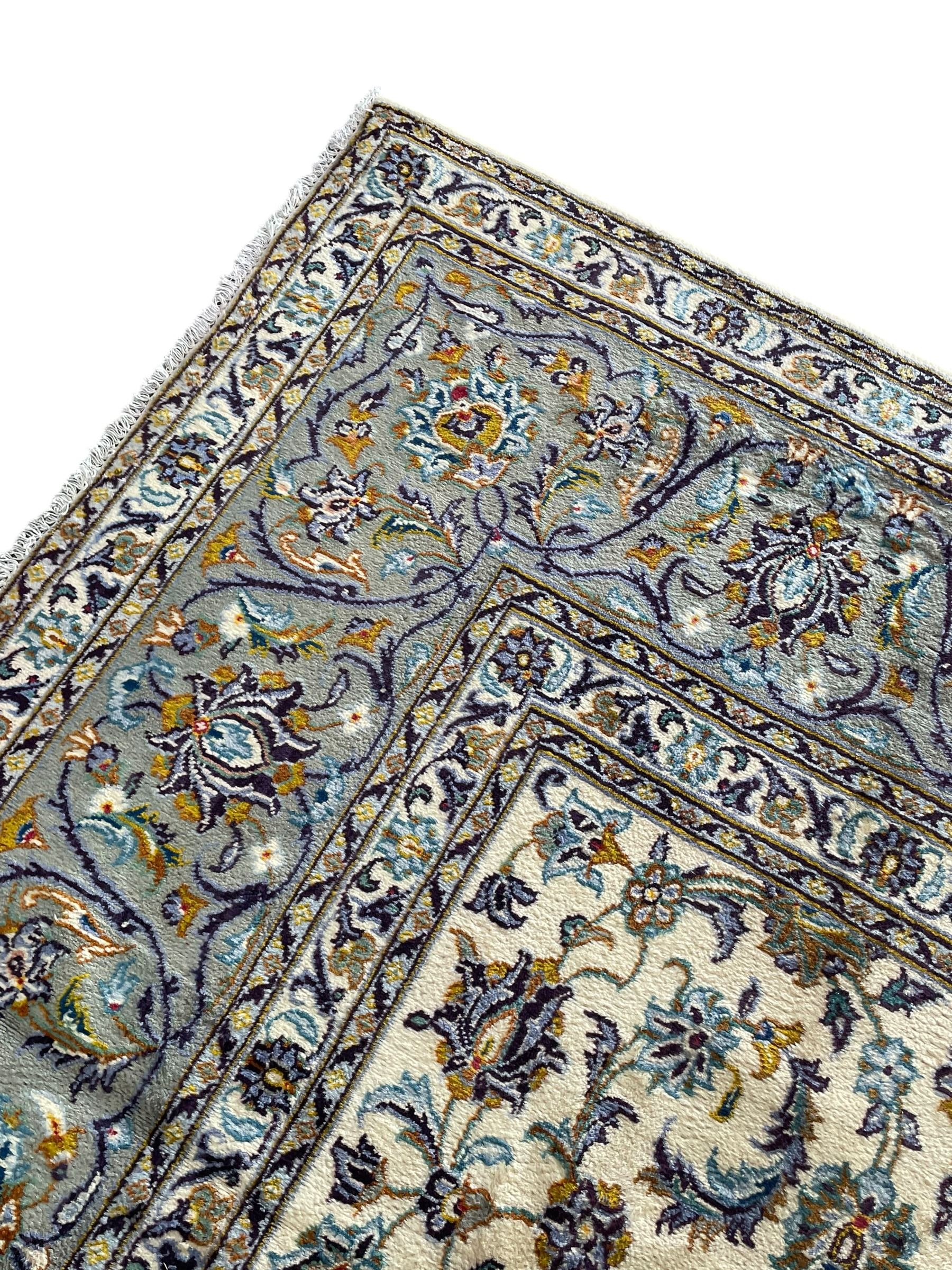 Persian Kashan ivory ground carpet, the busy field decorated with scrolling and interlaced leafy branches and palmettes, trailing branch border with repeating stylised plant motifs, within floral pattern guard stripes 