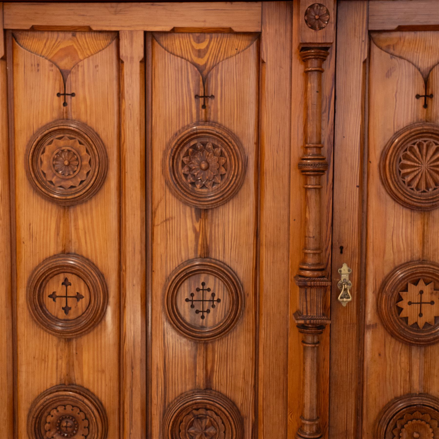 19th century pitch pine ecclesiastical vestment wardrobe or sacristy cabinet, crenelated and projecting moulded cornice over two panelled doors, the panelled doors carved with linen folds and mounted with rows of roundels depicting crucifixes and flower heads, enclosed by turned pilasters, two drawers to the base, on moulded plinth base 