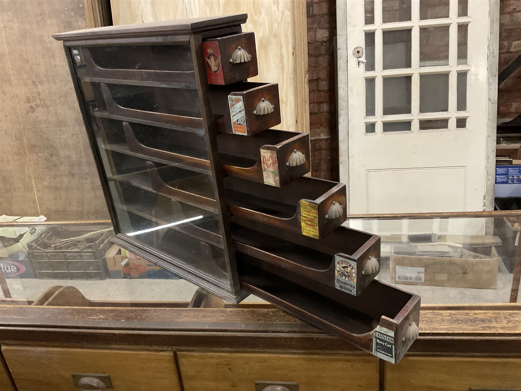 Early 20th stained pine and glazed wall mounting cigarette shop display cabinet, fitted with six sliding drawers with divisions and scalloped handles  - THIS LOT IS TO BE COLLECTED BY APPOINTMENT FROM THE OLD BUFFER DEPOT, MELBOURNE PLACE, SOWERBY, THIRSK, YO7 1QY