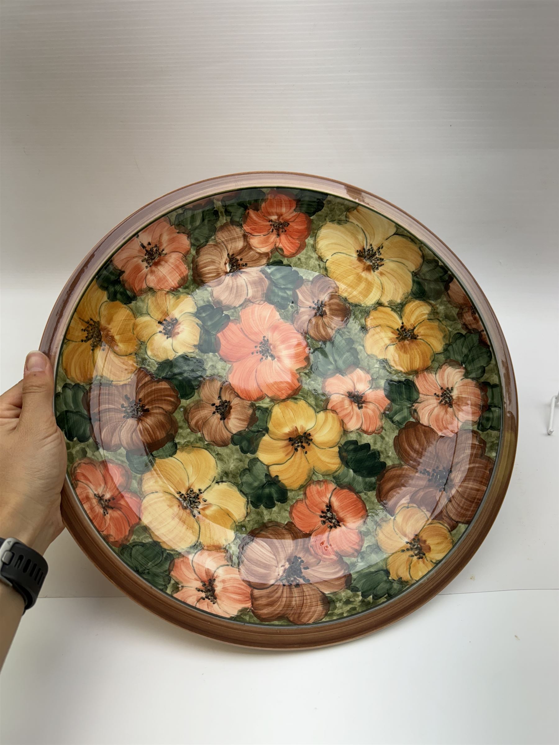 Two Gray's pottery charges, decorated with flowers, together with another charger by Jersey pottery