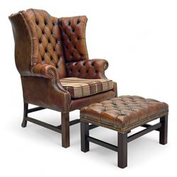 Georgian design hardwood-framed wingback armchair, shaped cresting rail and deep wingback over rolled arms, upholstered in brown buttoned leather with studwork bands, the seat cushion upholstered in checkered fabric, on square supports united by stretchers (W86cm, H118cm, D86cm); together with matching rectangular footstool (63cm x 43cm, H37cm) 