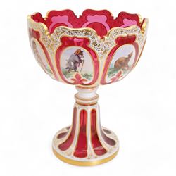 Late 19th century Bohemian white overlaid cranberry glass pedestal bowl, with fancy scalloped rim and cut with oval and fleur de lis shaped panels, each enamelled with 'Reynard the Fox' anthropomorphic animals, after the illustrations by Wiilhem Von Kaulbach,  within gold borders with gilt scrolling decoration, supported by a slice cut circular spreading foot with further gilt decoration, H28.5cm x W22.5cm