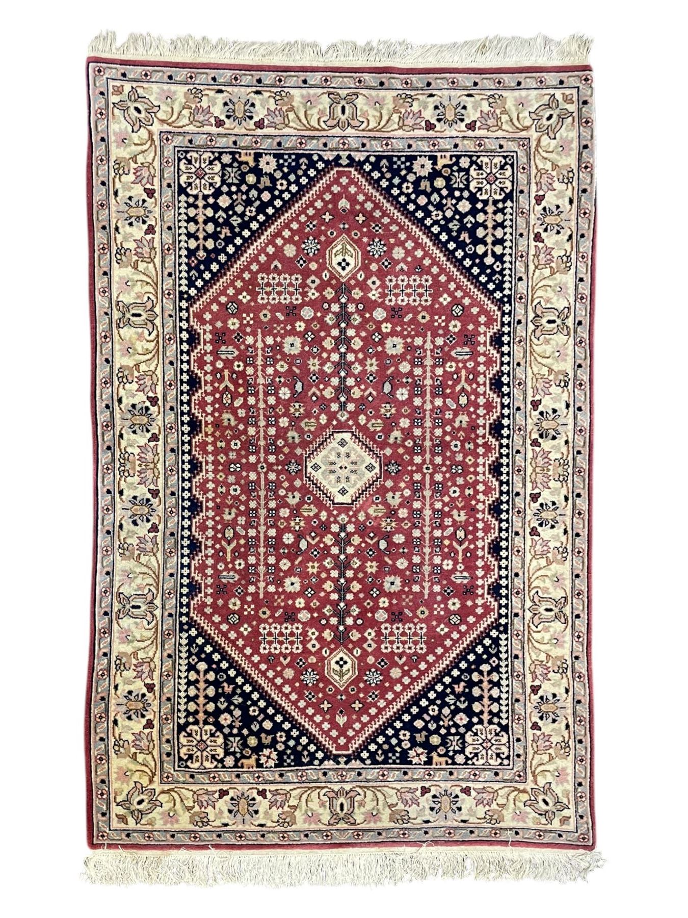 Persian design crimson ground rug, the field decorated with tree of life and floral motifs, enclosed by indigo spandrels with stylised flower head decoration, repeating scrolling border 