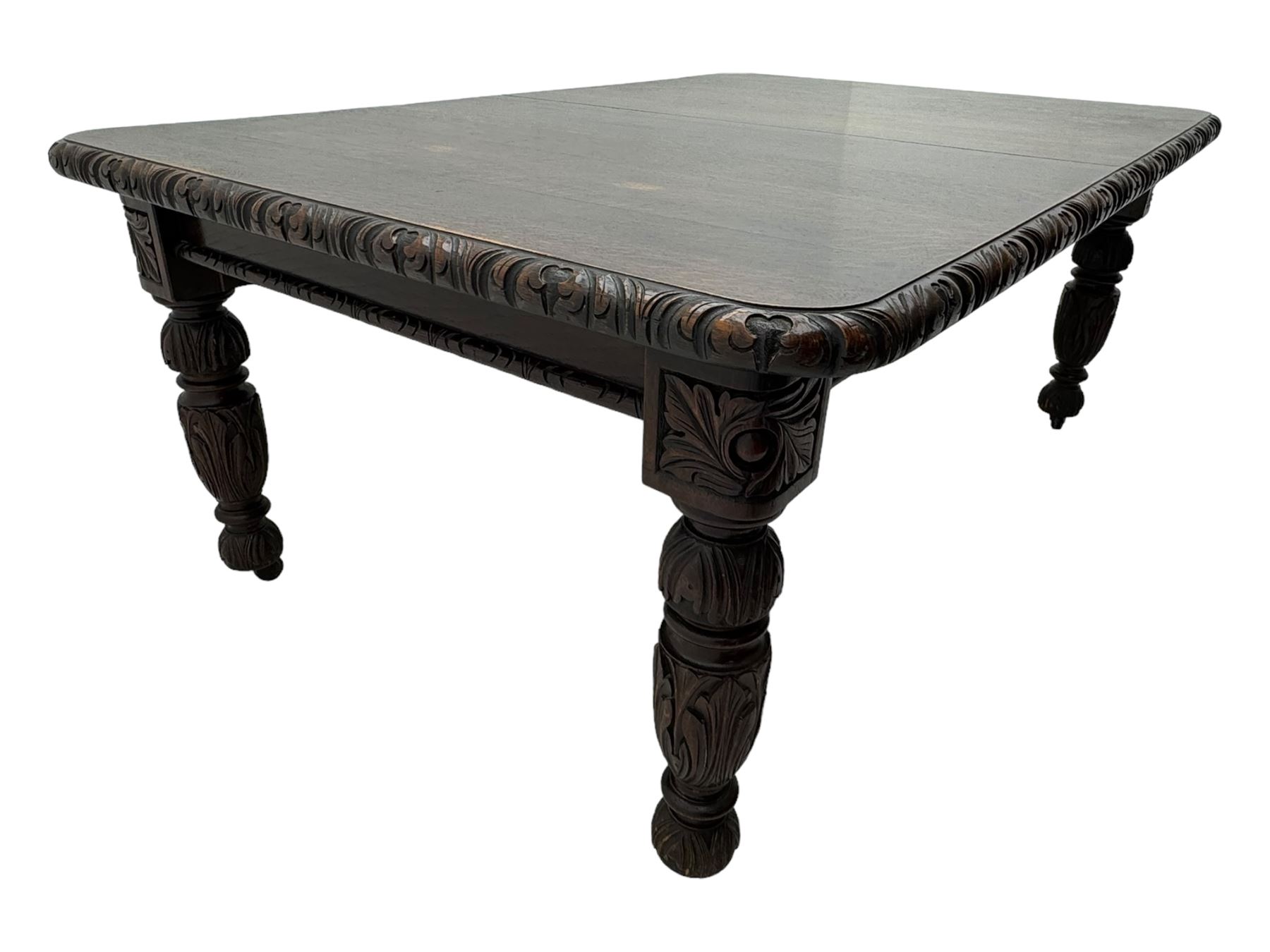 19th century heavily carved oak extending dining table, rectangular top with rounded corners and carved gadrooned edge, extending via winding mechanism with two additional leaves, raised on acanthus leaf-carved baluster supports terminating in ceramic castors