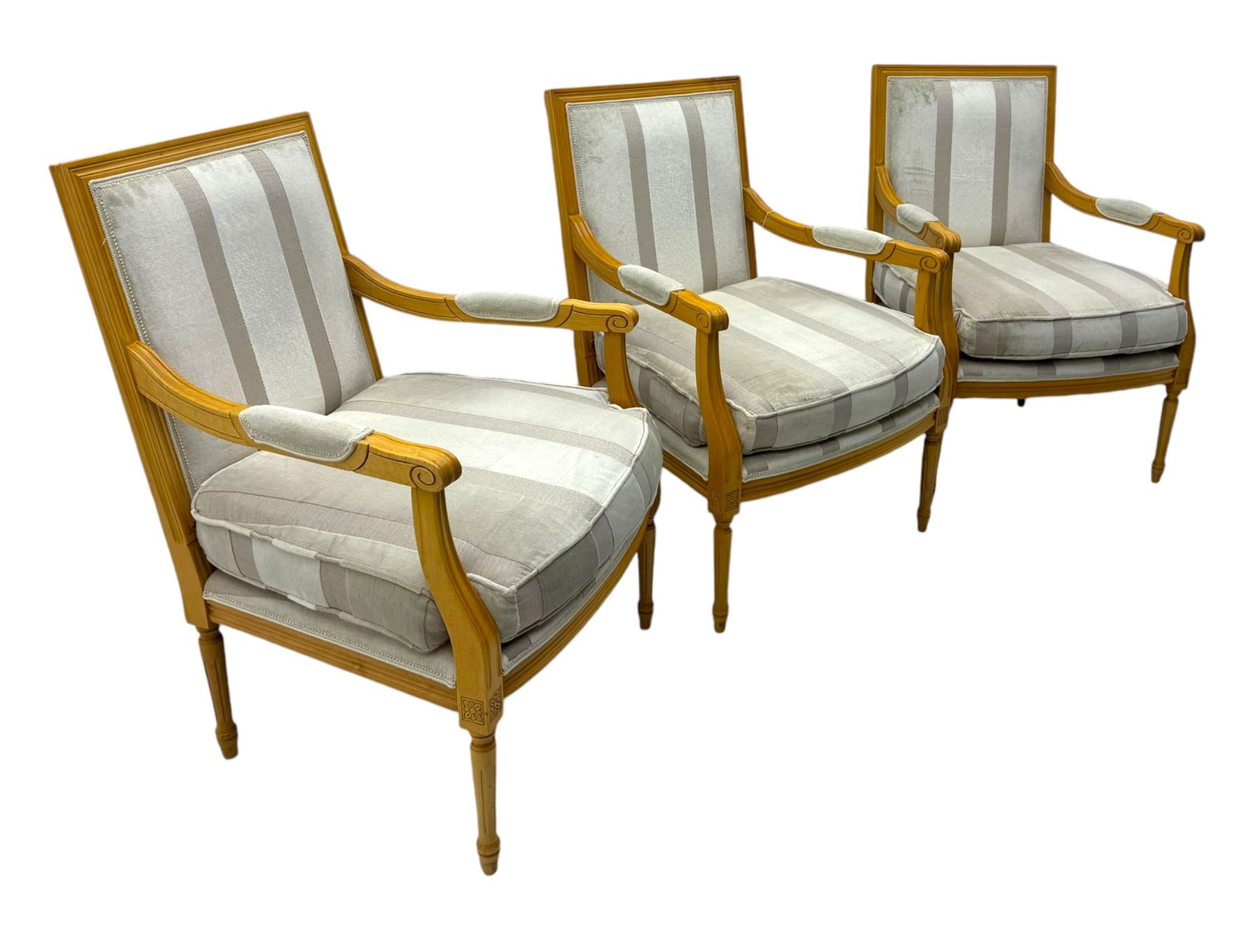 Three mid-20th century beechwood fauteuil armchairs, upholstered backrest and seat in cream stripe fabric, padded armrests with scroll detail, on tapered fluted supports with carved floral rosette blocks