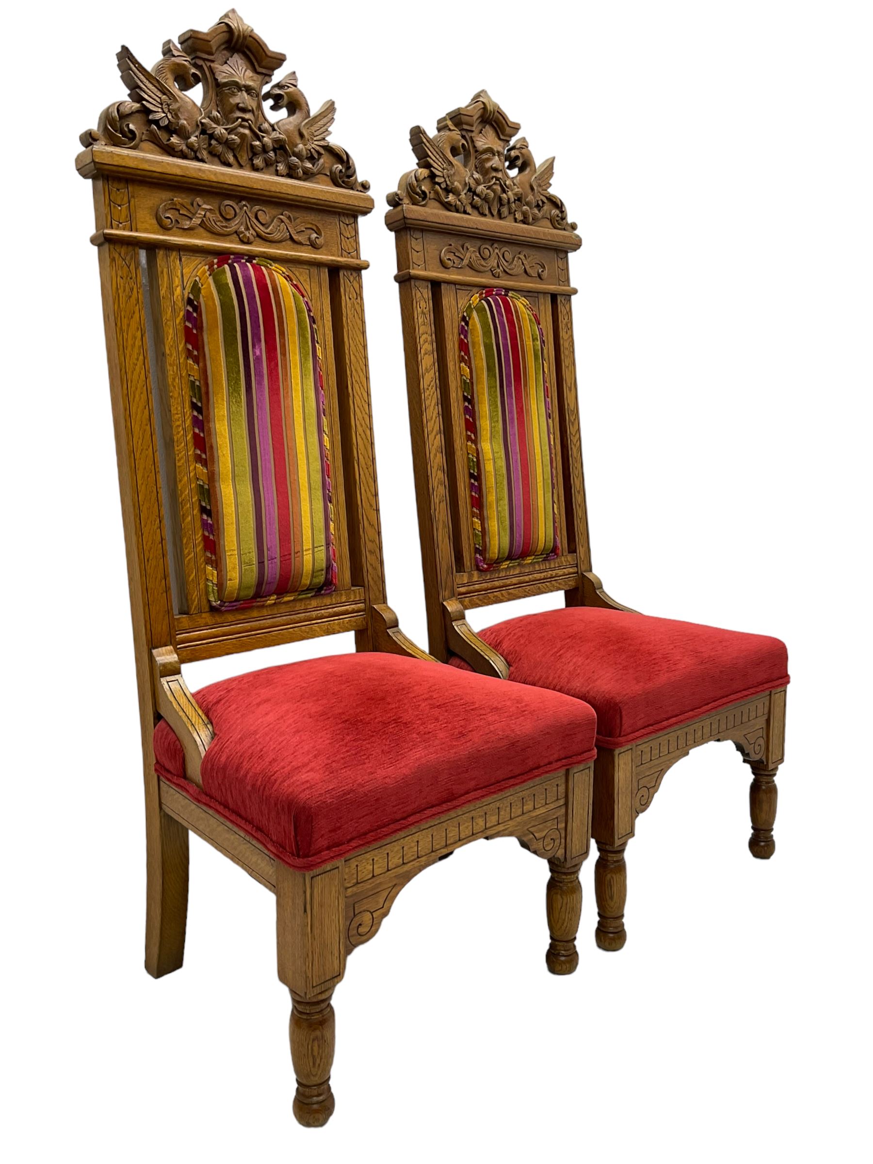 Set of six 20th century Carolean design oak high back chairs, the pediment carved with dragons and central Green Man mask with trailing foliage, the backs upholstered in striped fabric, on turned front supports