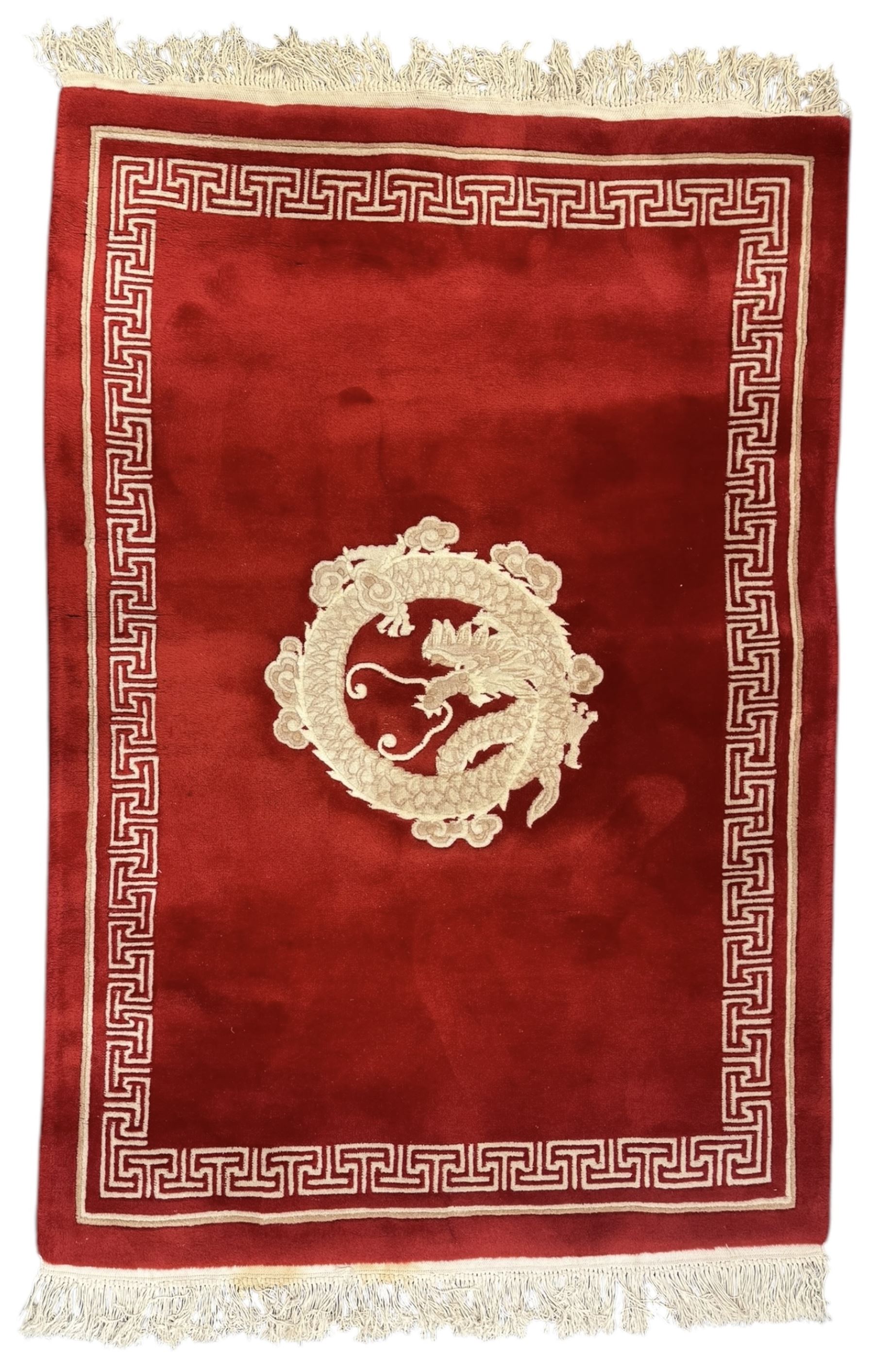 Chinese washed woolen red ground rug, central circular dragon motif in ivory, framed by a decorative Greek key border in matching ivory tones, finished with fringed ends