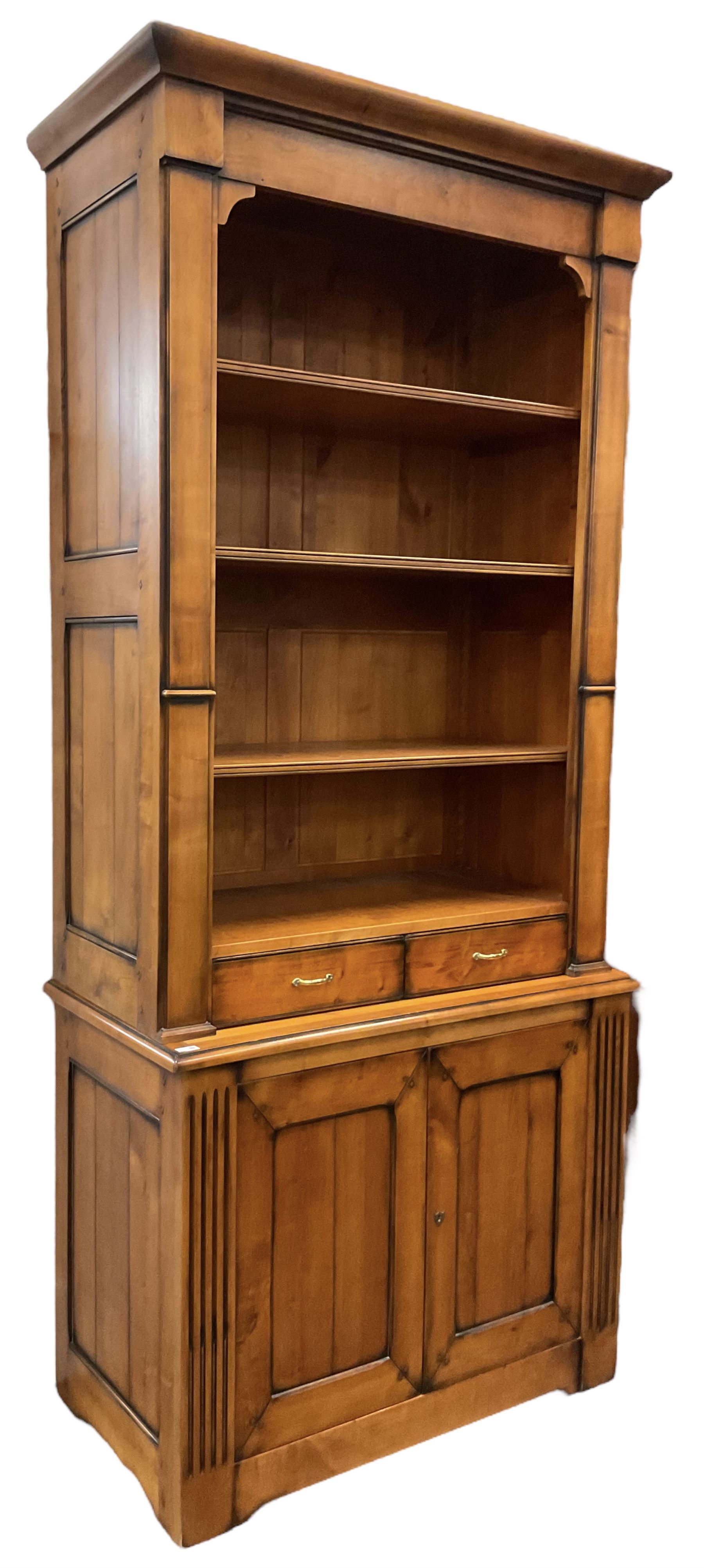 French cherry wood bookcase on cupboard, projecting moulded cornice over three shelves and two small drawers, the cupboard enclosed by two panelled doors flanked by fluted uprights