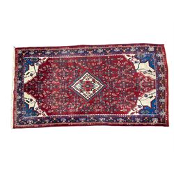 Persian Herati crimson ground rug, the busy field decorated with a central lozenge medallion surrounded by interlocking Herati motifs, the indigo guard band with repeating palmette and stylised plant motifs