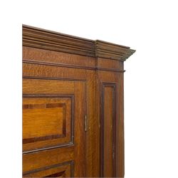 George III and later oak and mahogany banded corner cupboard, moulded cornice over four panelled doors, the door panels inlaid with mahogany bands, projecting square pilasters throughout with applied reeded mouldings, the painted interior fitted with shaped shelves, on moulded plinth base 