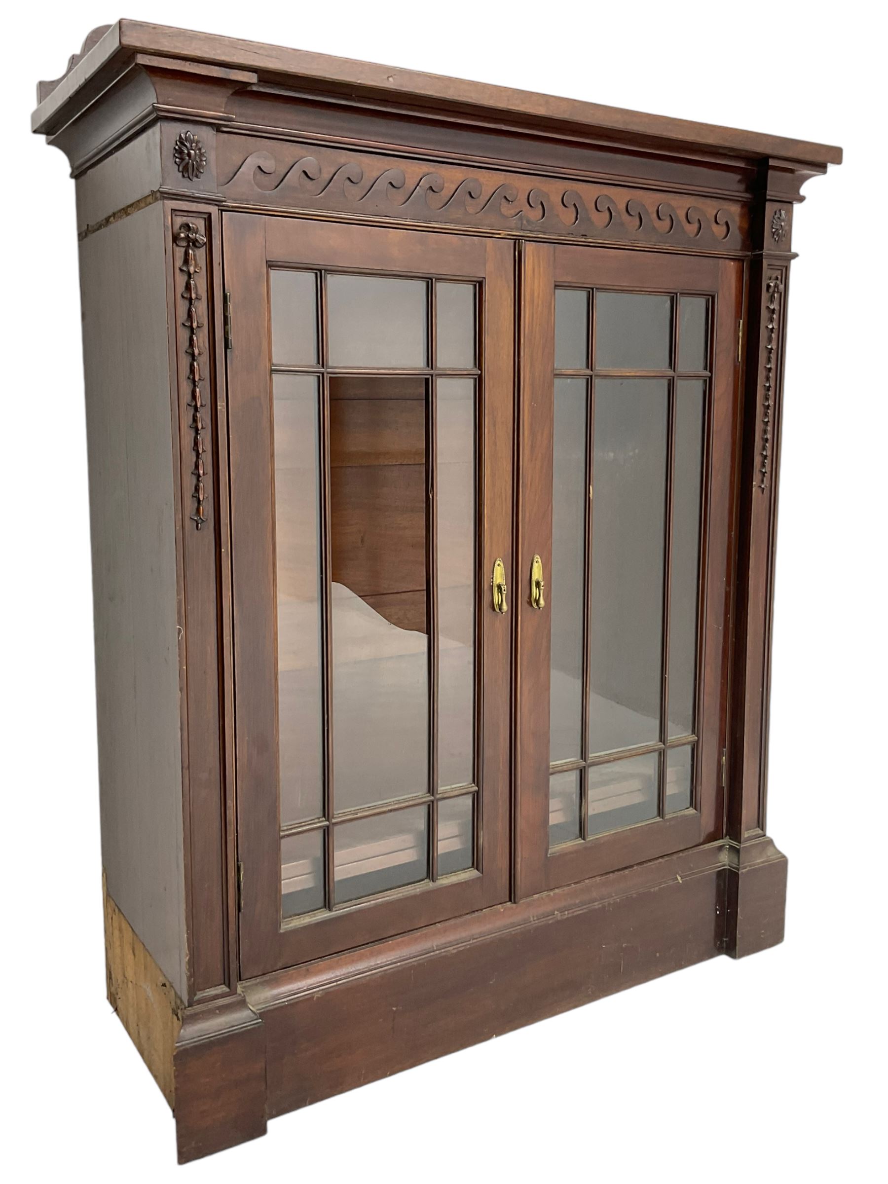 19th century mahogany display cabinet, rectangular top over frieze decorated with Vitruvian scroll mount, enclosed by two astragal glazed doors, the upright rails decorated with trailing bellflowers, on moulded plinth