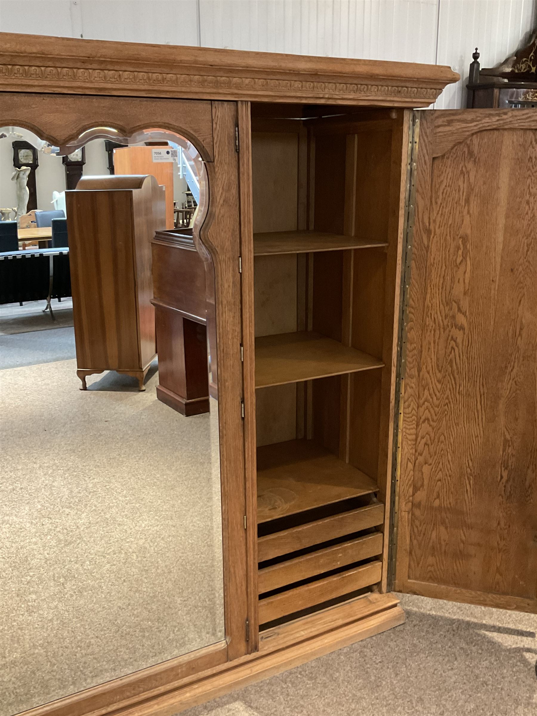 Late 19th century oak triple wardrobe, wide central bevelled mirror door, flanked by two panelled doors each carved with scrolling leaves and flower heads, on moulded skirt base 