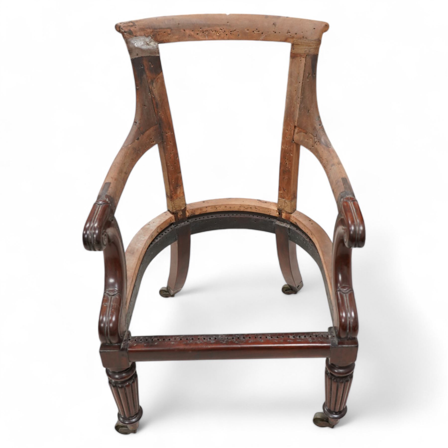 Regency mahogany and hardwood-framed library chair, curved and rolled cresting rail over scroll and lappet carved arm terminals, on turned and reed carved supports with brass castors 