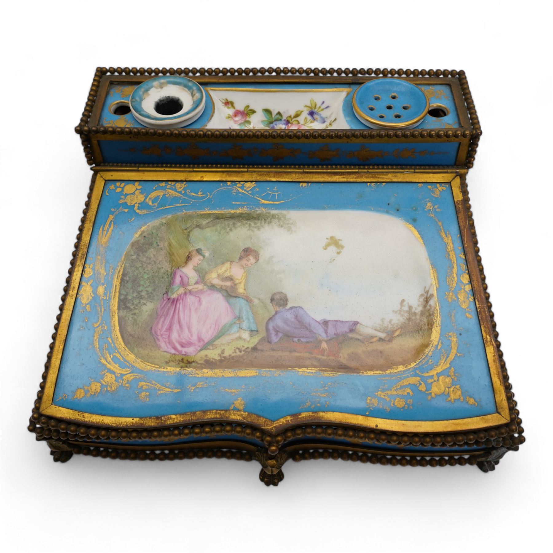 19th century French Sevres style porcelain and gilt brass table top writing box, the fall front painted with three figures in a woodland landscape, within a gilt border on a bleu celeste ground, the side panels depicting floral sprays, the top with removable porcelain inkwell and pounce pot, beaded gilt metal border with four lion paw supports and pink velvet fitted interior, L28cm x H14cm