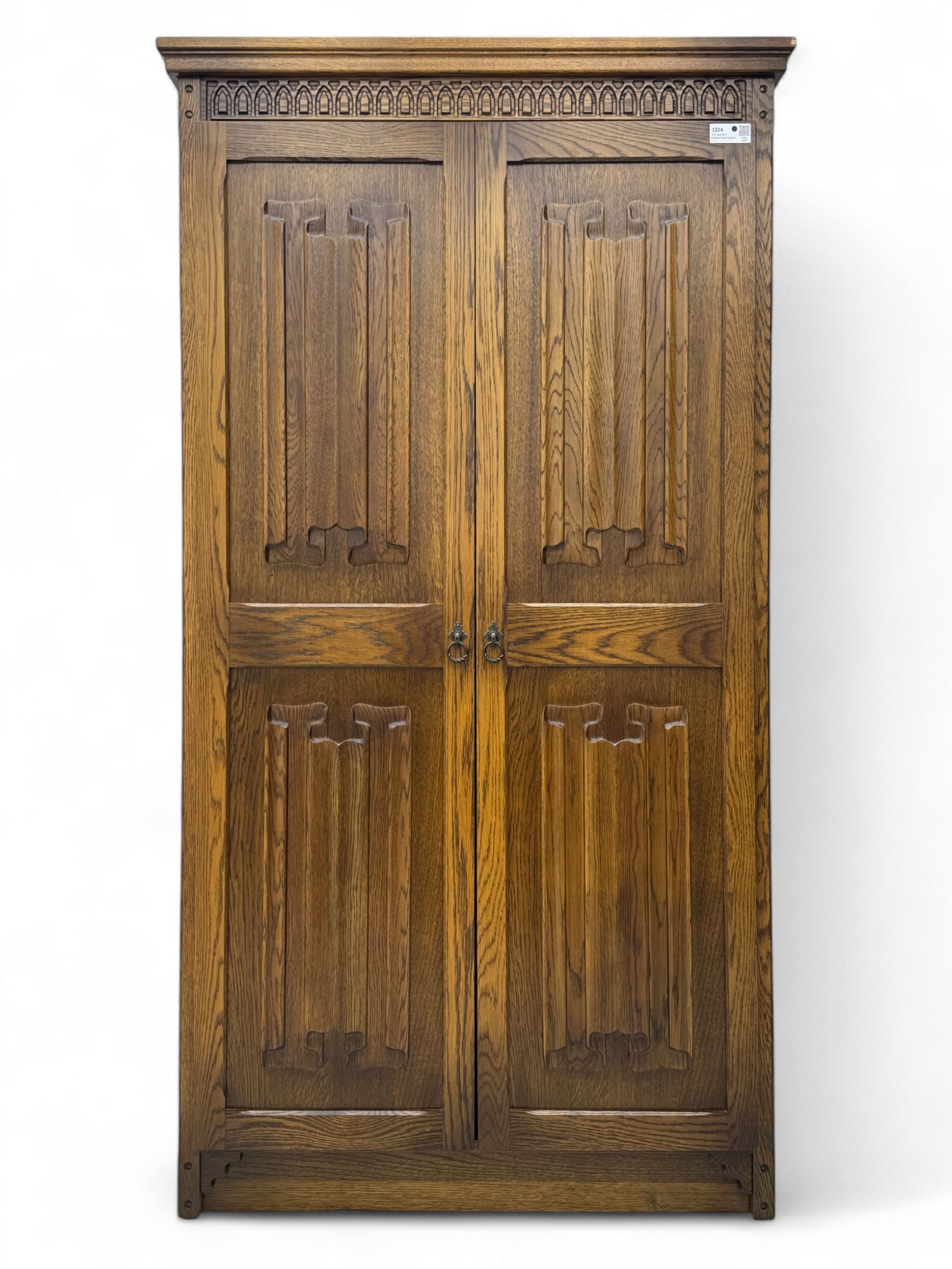 Jacobean design oak double wardrobe, projecting cornice over Gothic arched tracery carved frieze, twin panelled doors with linenfold relief carved detailing, on plinth base