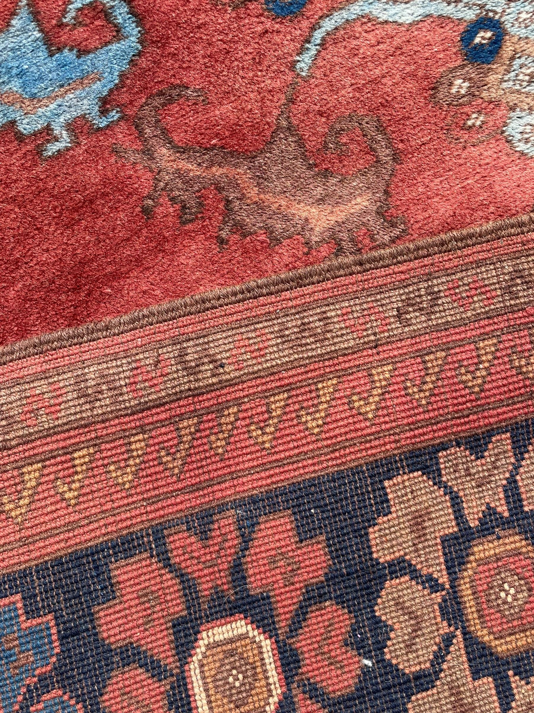 Afghan rust ground carpet, large central lozenge medallion decorated with stylised plant motifs, running water guard stripes enclosing indigo ground border decorated with stylised flower heads