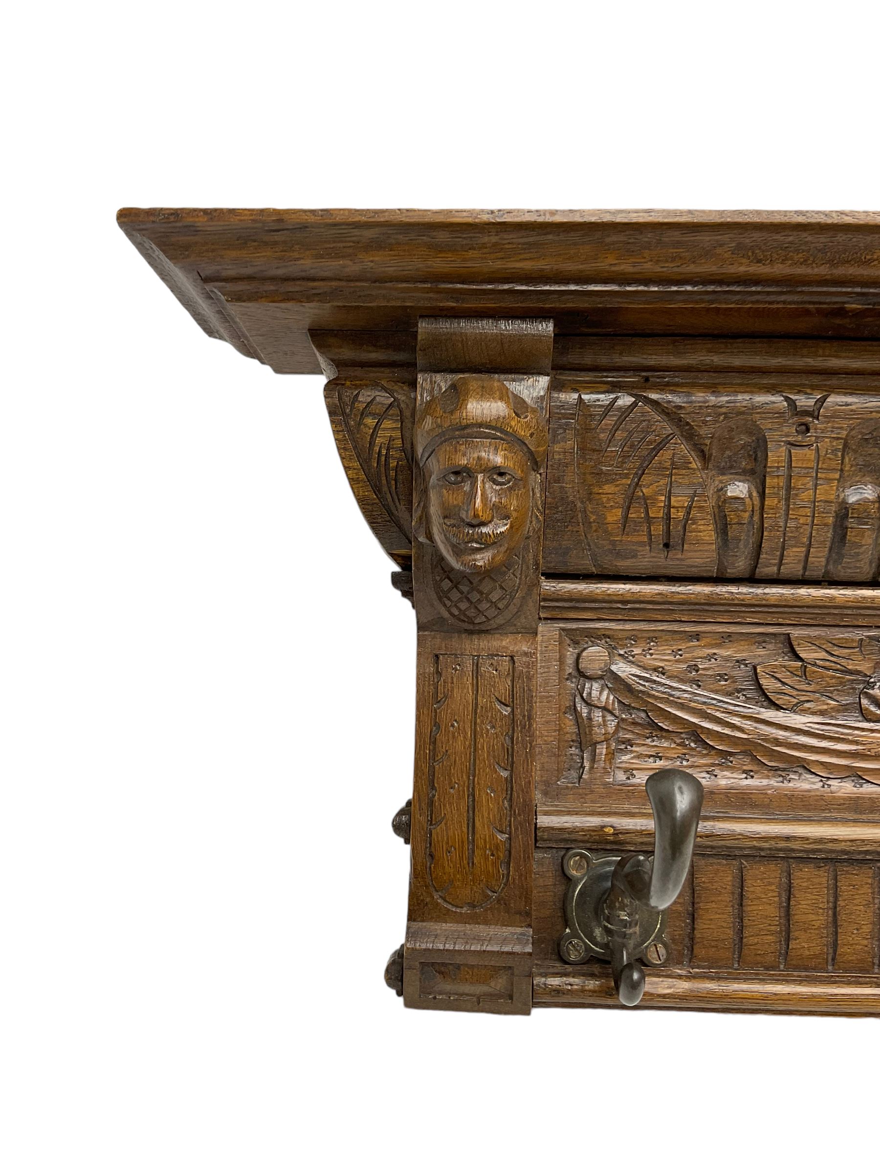 Late 20th century carved oak wall hanging coat rack, projecting moulded lintel over arcade carved frieze, flanked by two carved masks, fitted with five foliate cast hooks