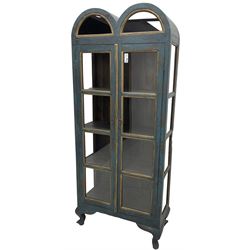 Tall painted glazed display cabinet, double arched top over two glazed doors, fitted with three shelves, in rustic blue paint finish, on cabriole feet