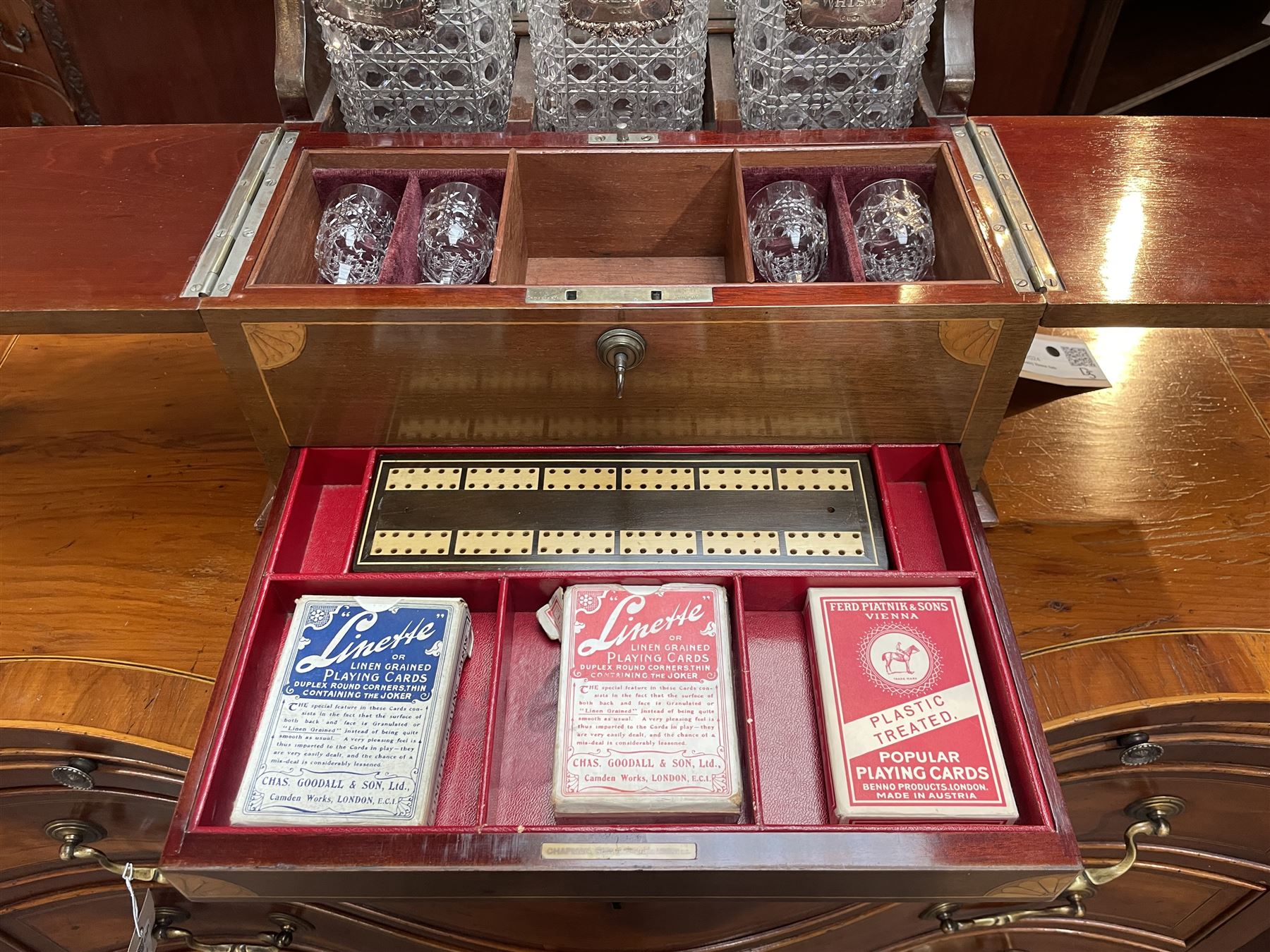 Edwardian walnut and boxwood inlaid tantalus games compendium, having three square section cut glass decanters, with associated silver Brandy, Sherry and Whisky labels, the two hinged doors with Bramah lock, open to reveal a fitted interior with four sherry glasses, over a secret sprung drawer to the base containing a selection of playing cards and cribbage board, L36cm x H32cm 