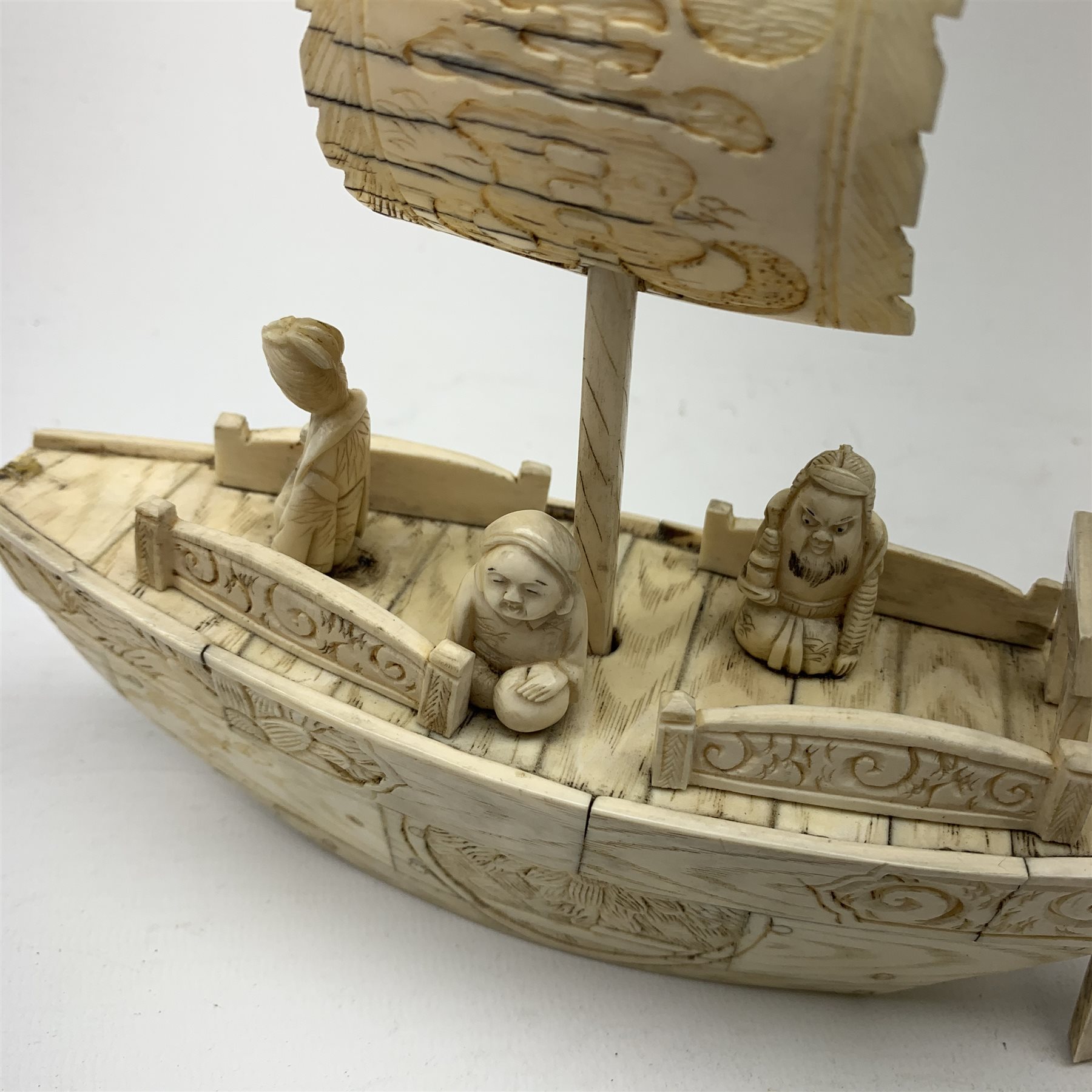 A Japanese carved ivory model of a sailing boat, surmounted by three carved figures (a/f), L22.5cm, together with a smaller sail boat with malachite hull and ivory sails and rudder, H18cm. 