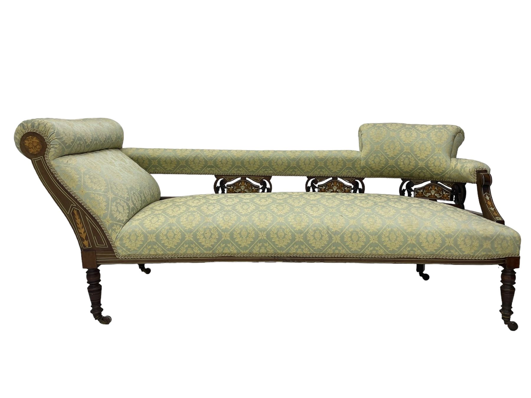 Late Victorian walnut salon settee or chaise lounge, double-ended with rolled back and curved end, upholstered in light aquamarine fabric with raised repeating lozenge pattern, decorated with laurel leaf wreaths and urns, three pierced splats carved with curled leaves, inlaid with dolphins and scrolled foliate motifs in simulated ivory and boxwood, on tapering ring turned supports with brass and ceramic castors (L166, D60, H70cm); together with matching tub-shaped armchair (W61cm, H73cm, D66cm)  