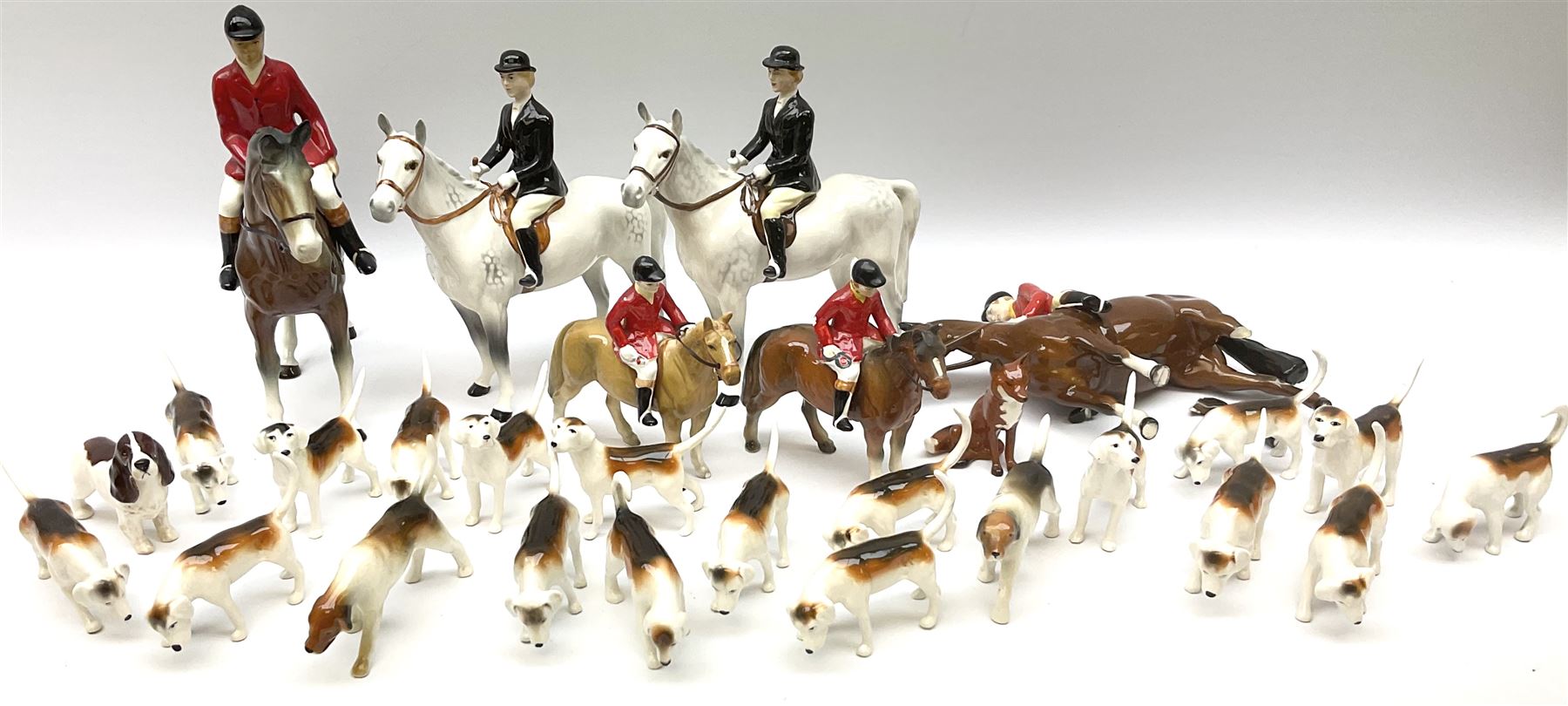 Beswick Hunting Group, comprising: two huntswoman on grey horses, model no 1730, huntsman on a bay horse, model no 1501, a seated fox, model no 1748, eighteen fox hounds and a spaniel, model no 967, all with printed marks beneath, together with three other ceramic huntsman on horseback and two hounds. 