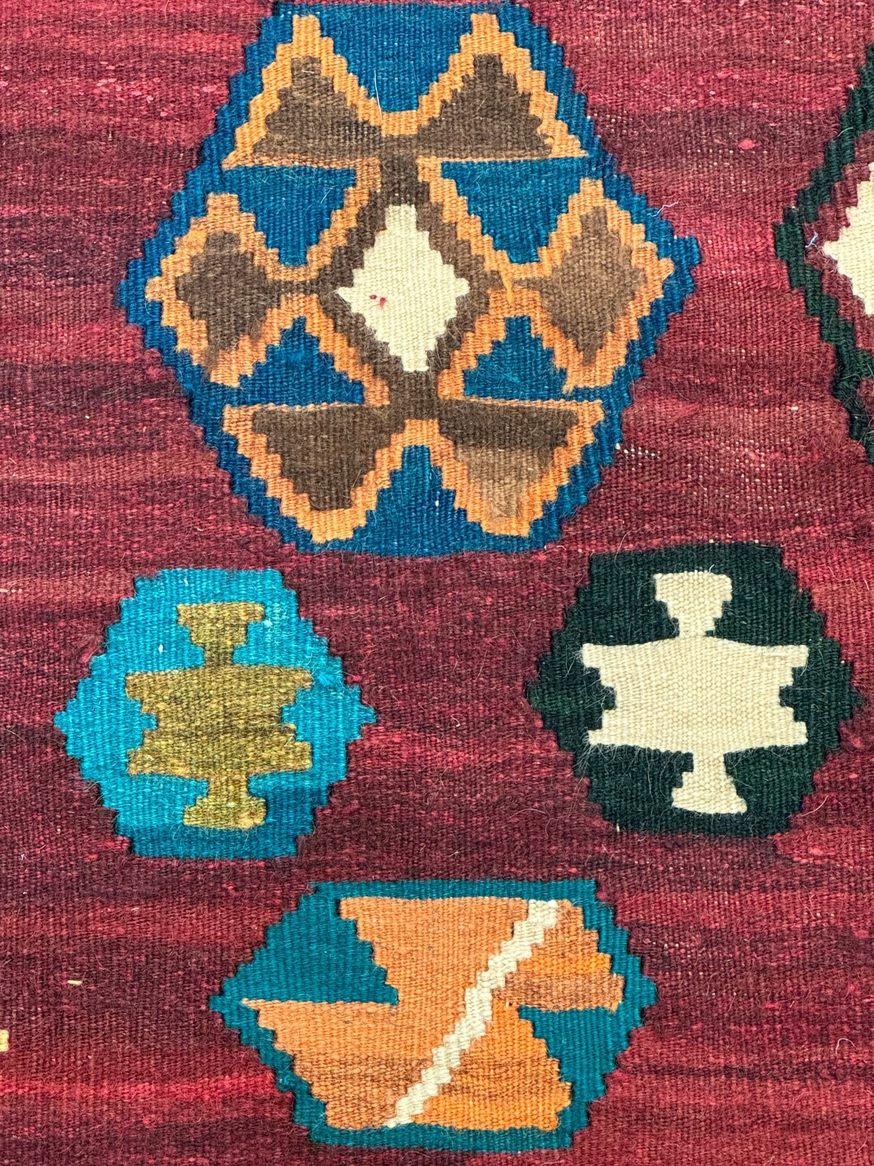 South West Persian Qashqai Kilim, crimson ground and decorated with three rows of geometric motifs, within zig-zag borders 