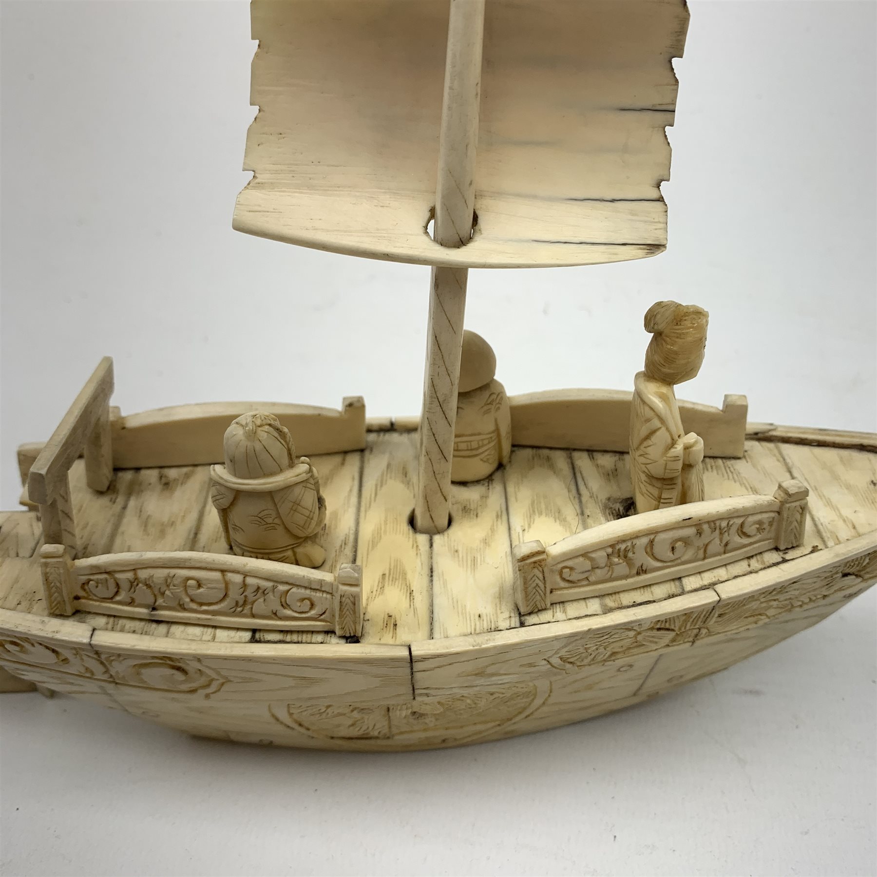 A Japanese carved ivory model of a sailing boat, surmounted by three carved figures (a/f), L22.5cm, together with a smaller sail boat with malachite hull and ivory sails and rudder, H18cm. 