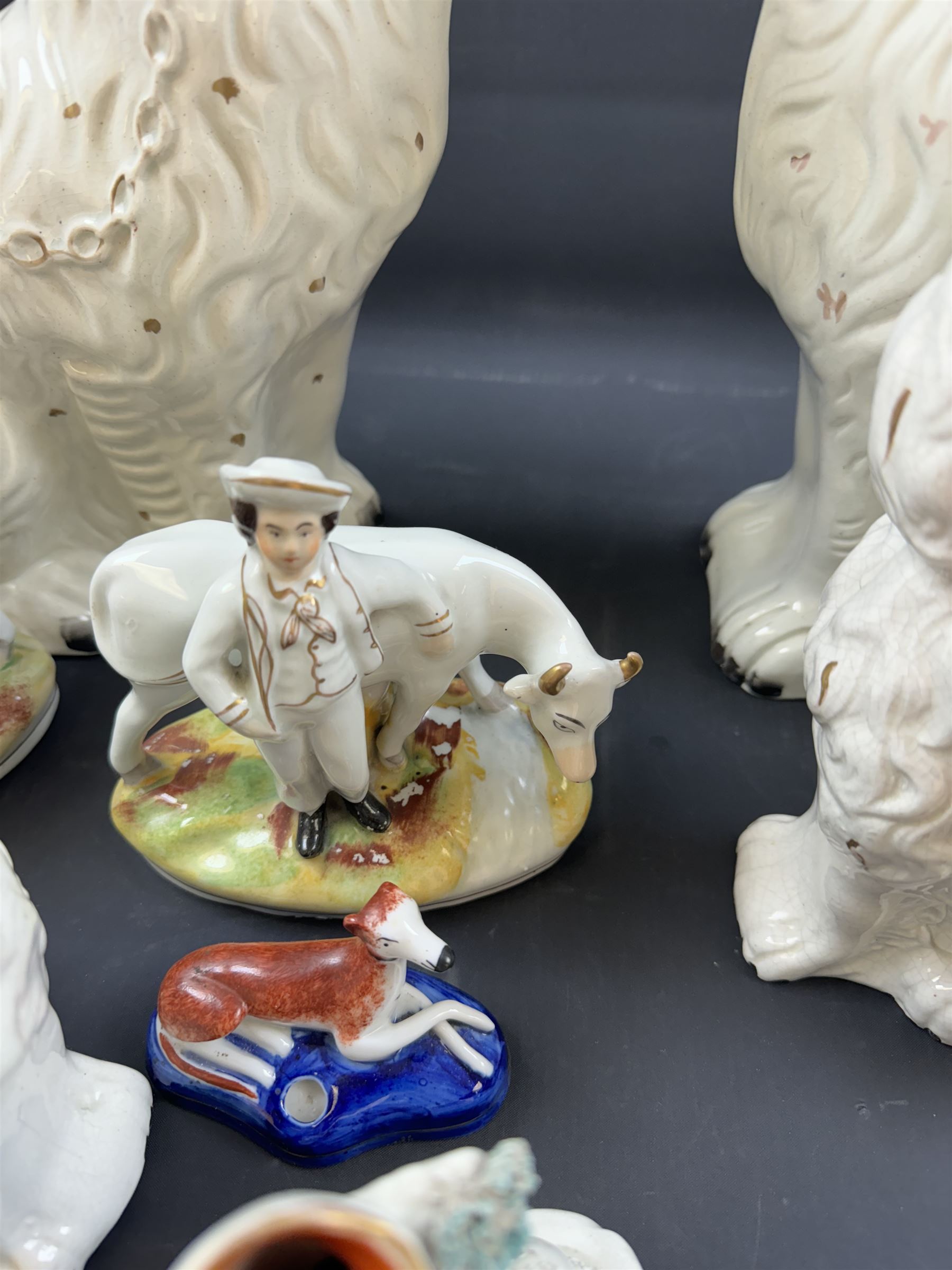 Staffordshire and Staffordshire style figures, to include a chained hound upon a blue oval base in the manner of Samuel Alcock, two pairs of seated Spaniels, a pair modelled as male figure and milk maid with cows, pair of recumbent Greyhounds, etc.