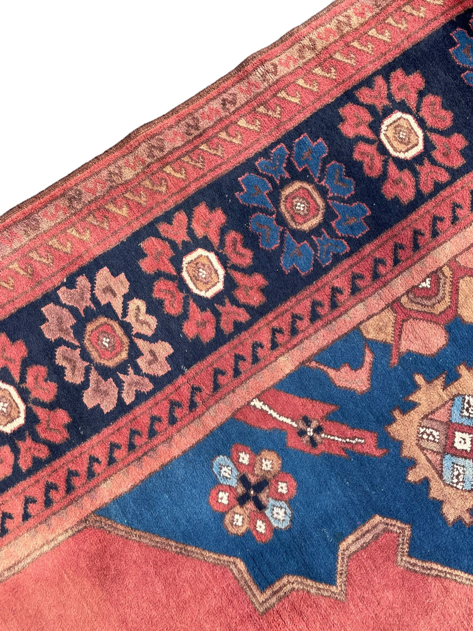 Afghan rust ground carpet, large central lozenge medallion decorated with stylised plant motifs, running water guard stripes enclosing indigo ground border decorated with stylised flower heads