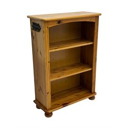 Traditional pine open bookcase, featuring arched top section flanked by fluted side supports, two adjustable shelves and cast iron coat hook with cat motif to the left side, standing on round bun feet 